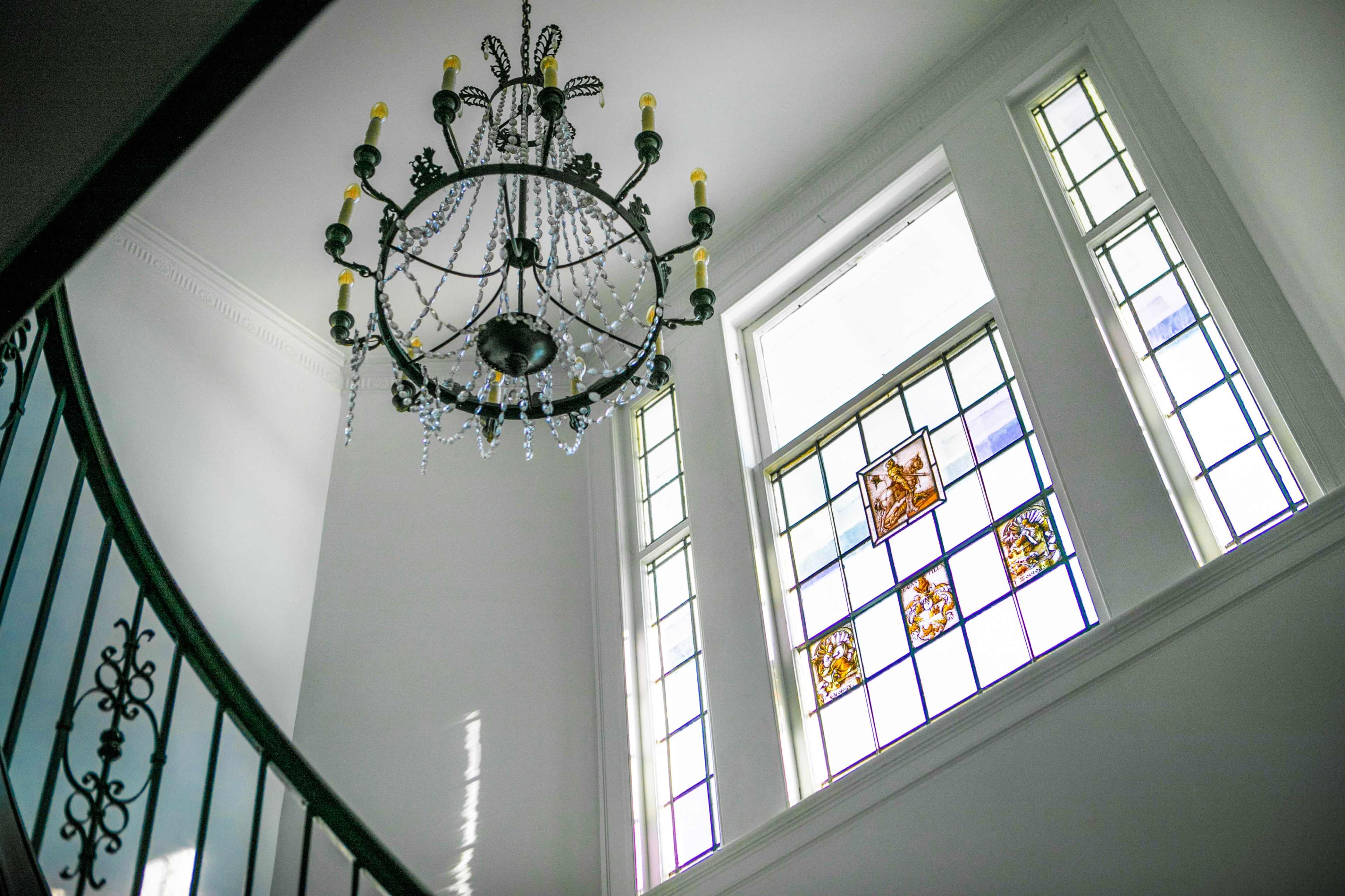 The image shows a staircase under a chandelier with stained glass windows illuminating the space.