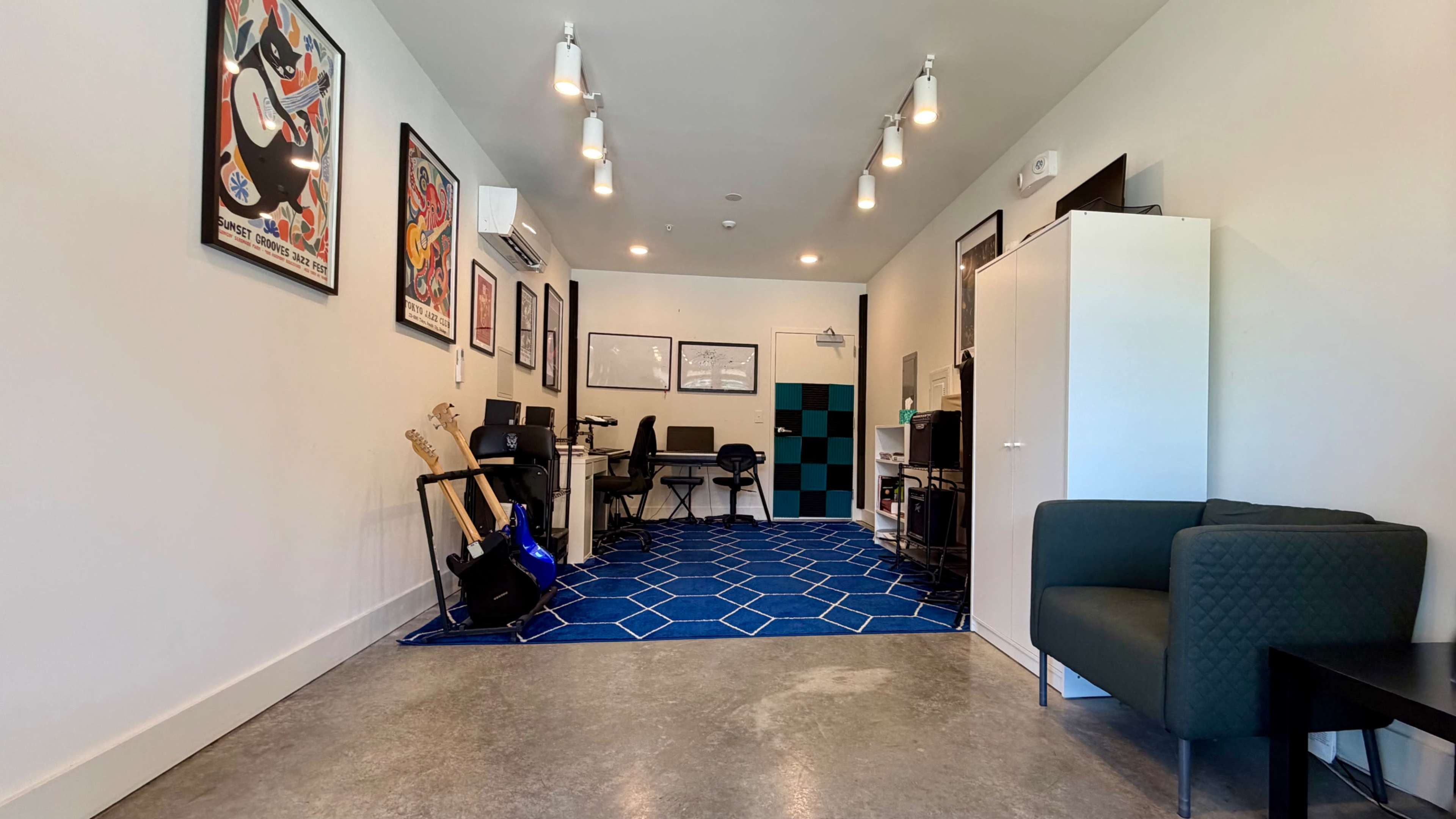 The image shows a modern room with musical instruments, including guitars, desks, and artwork on the walls, along with blue carpeting and various furniture.