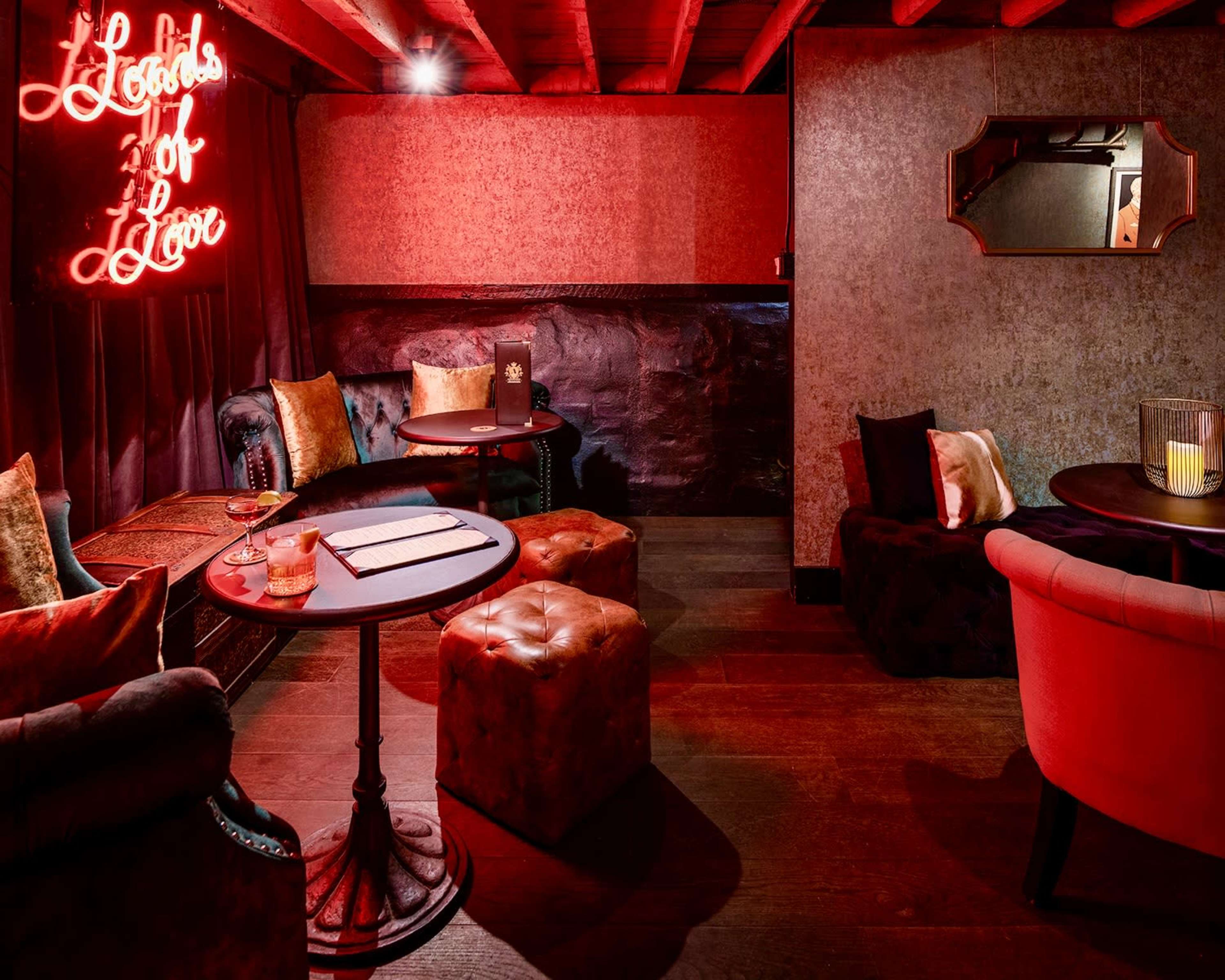 A dimly lit lounge area with plush seating, small round tables, and a neon sign reading "Lobbies for Love."
