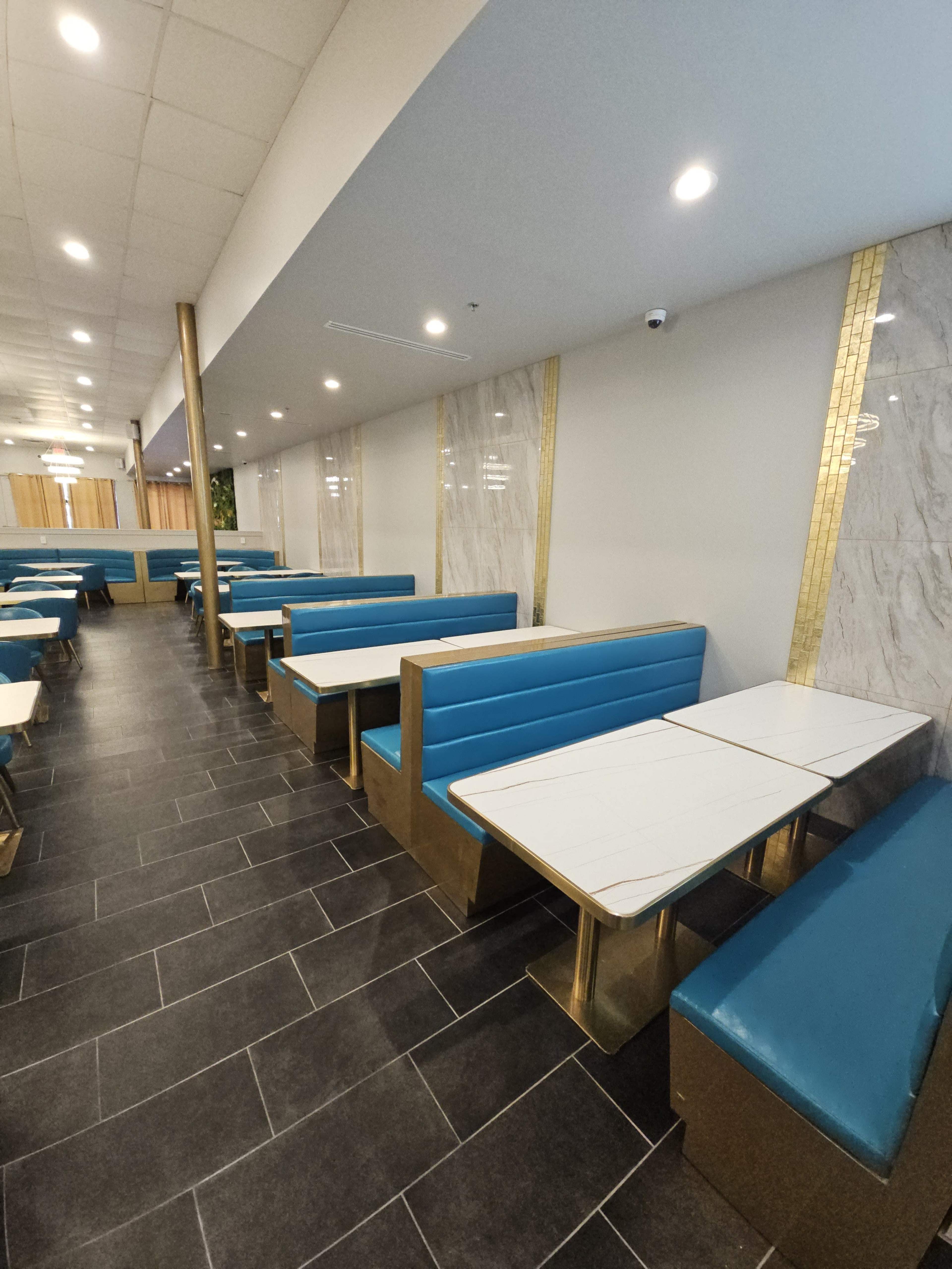 A modern restaurant interior features blue upholstered booths and marble accents, with a long row of tables arranged along the walls.