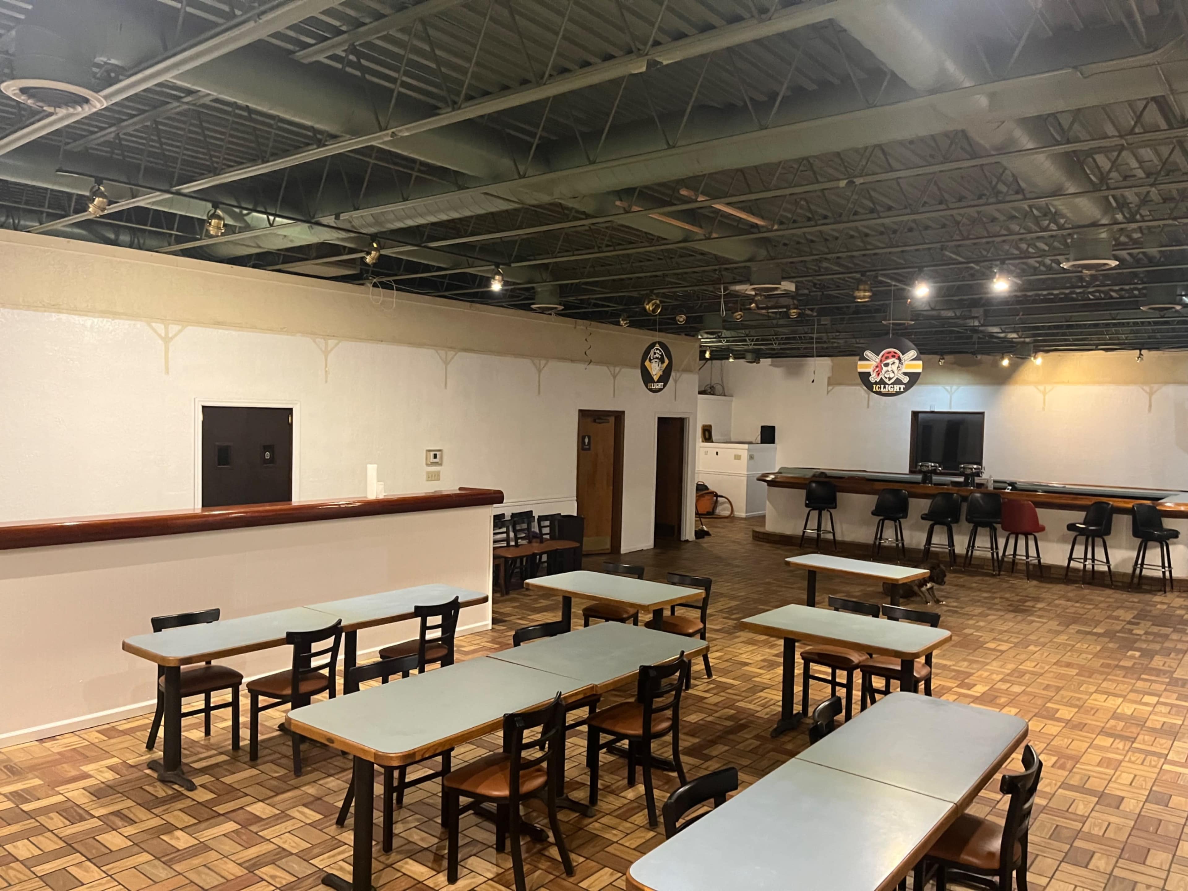 The image shows a spacious, empty dining area with several tables and chairs arranged on a patterned tile floor, along with a service counter against one wall.