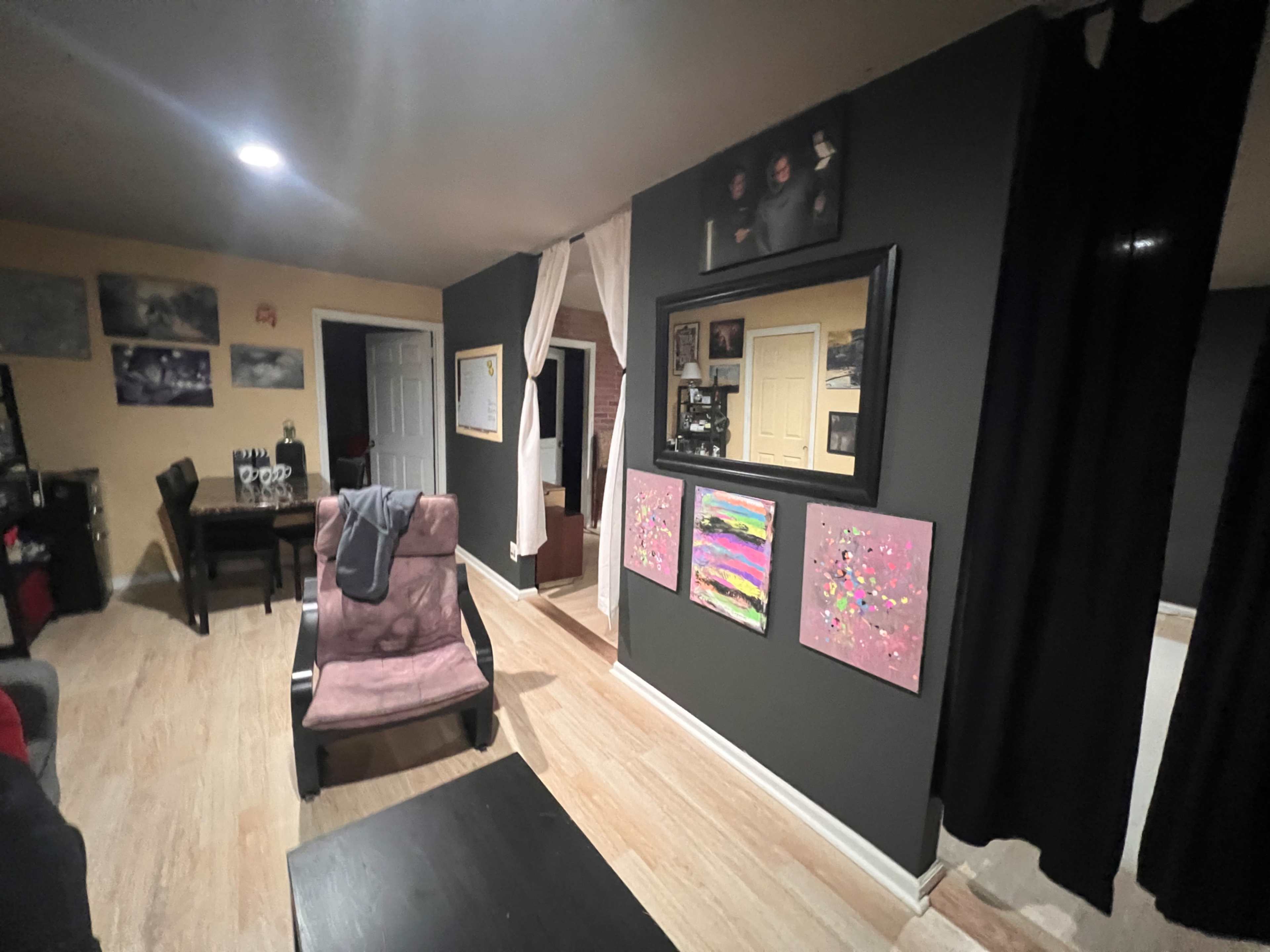 A dimly lit living room featuring a pink chair, a table, and several framed artworks on the wall.
