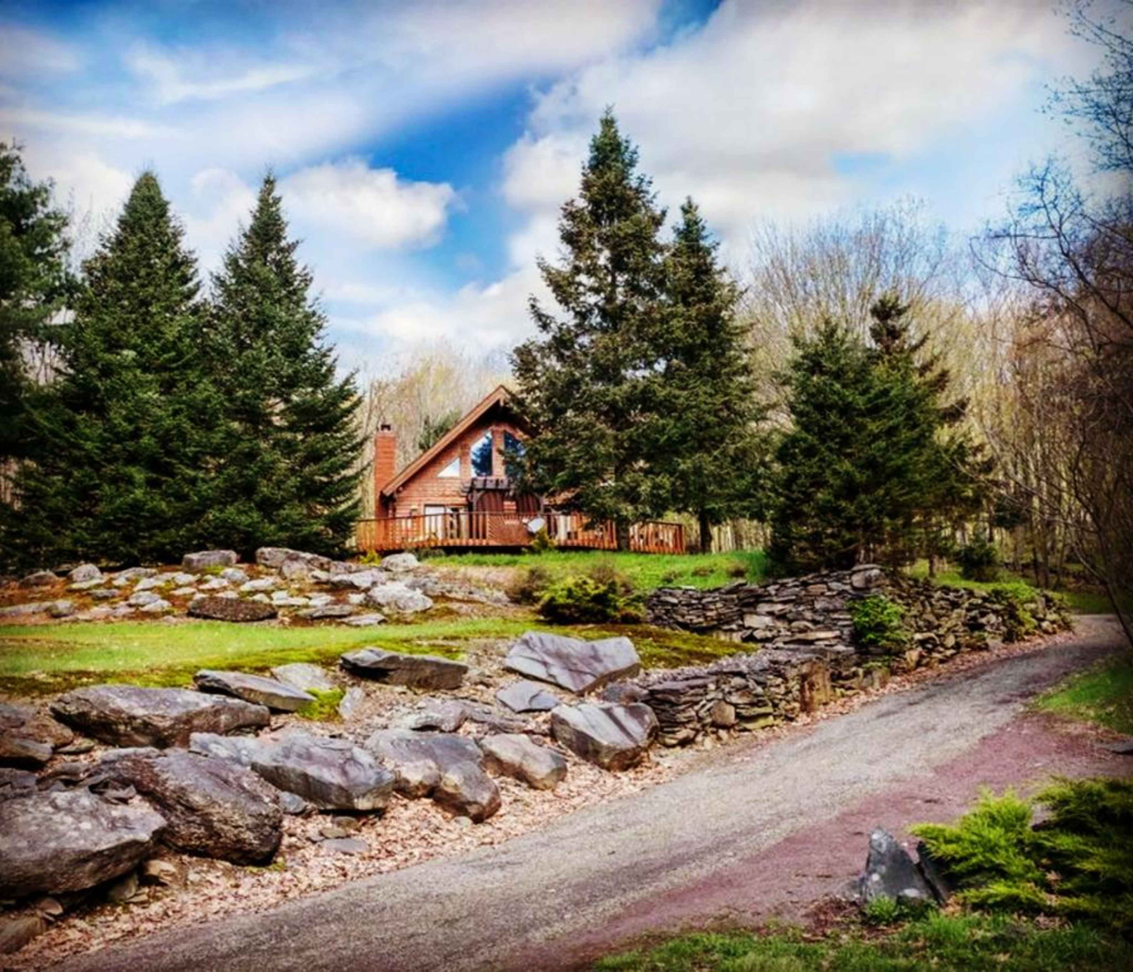 A gravel path leads to a wooden cabin among large rocks and tall evergreen trees.