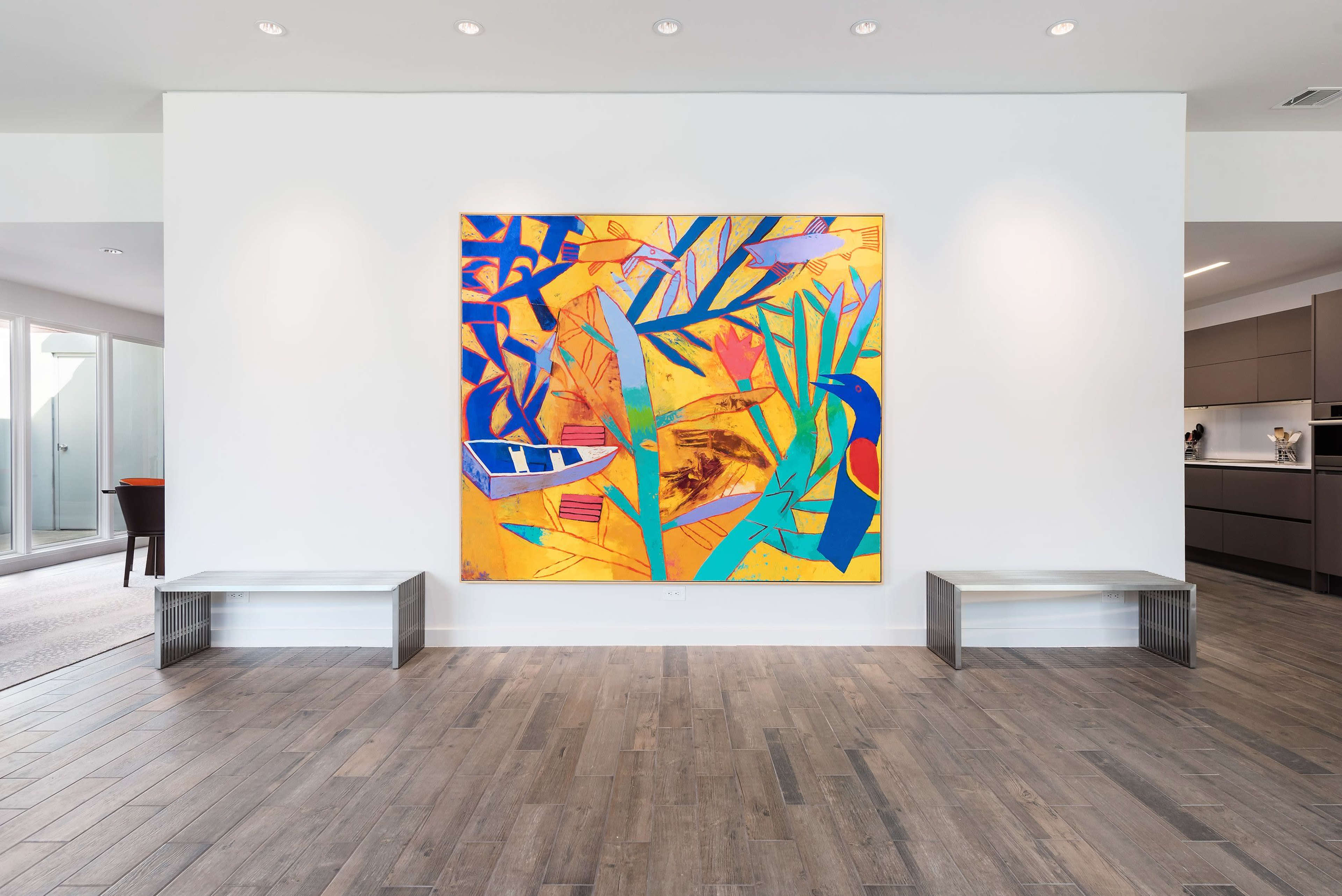A large, colorful abstract painting hangs on a white wall in a modern room with wooden flooring and minimalist furniture.