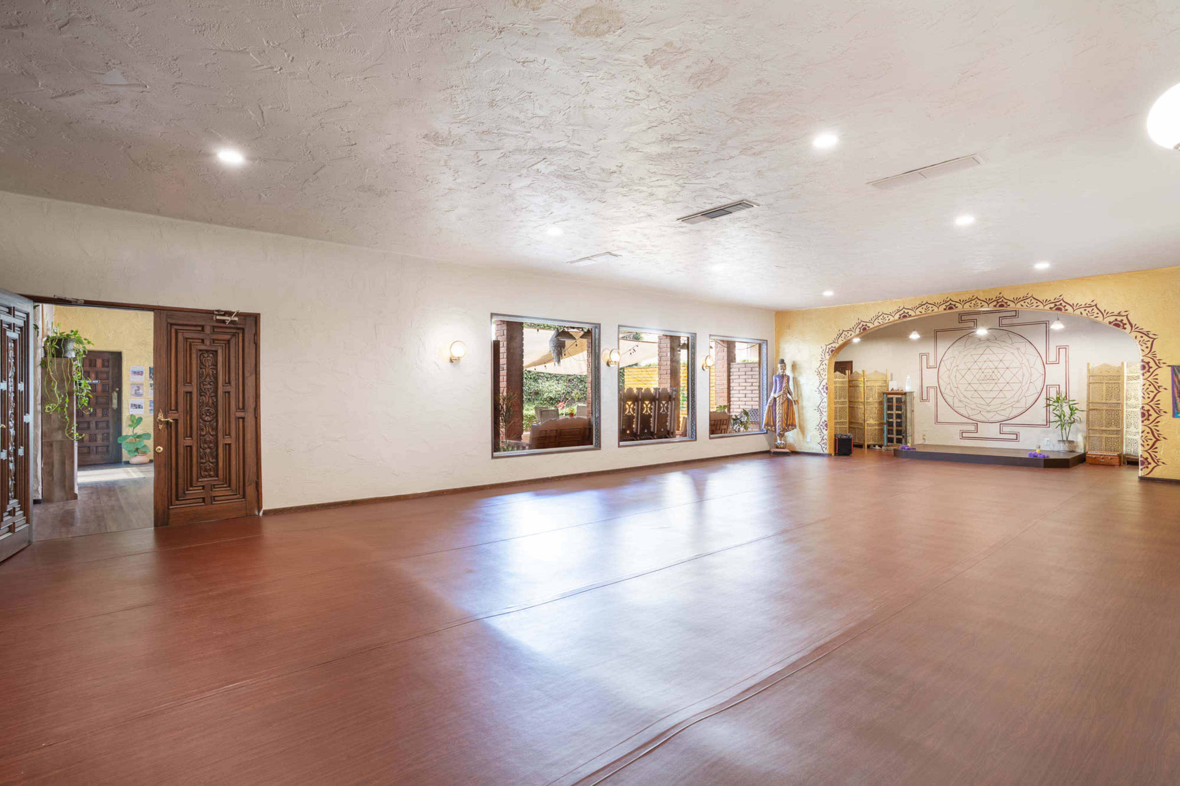 A spacious, well-lit studio features wooden flooring, large windows, and decorative wall art, creating an open and inviting atmosphere.