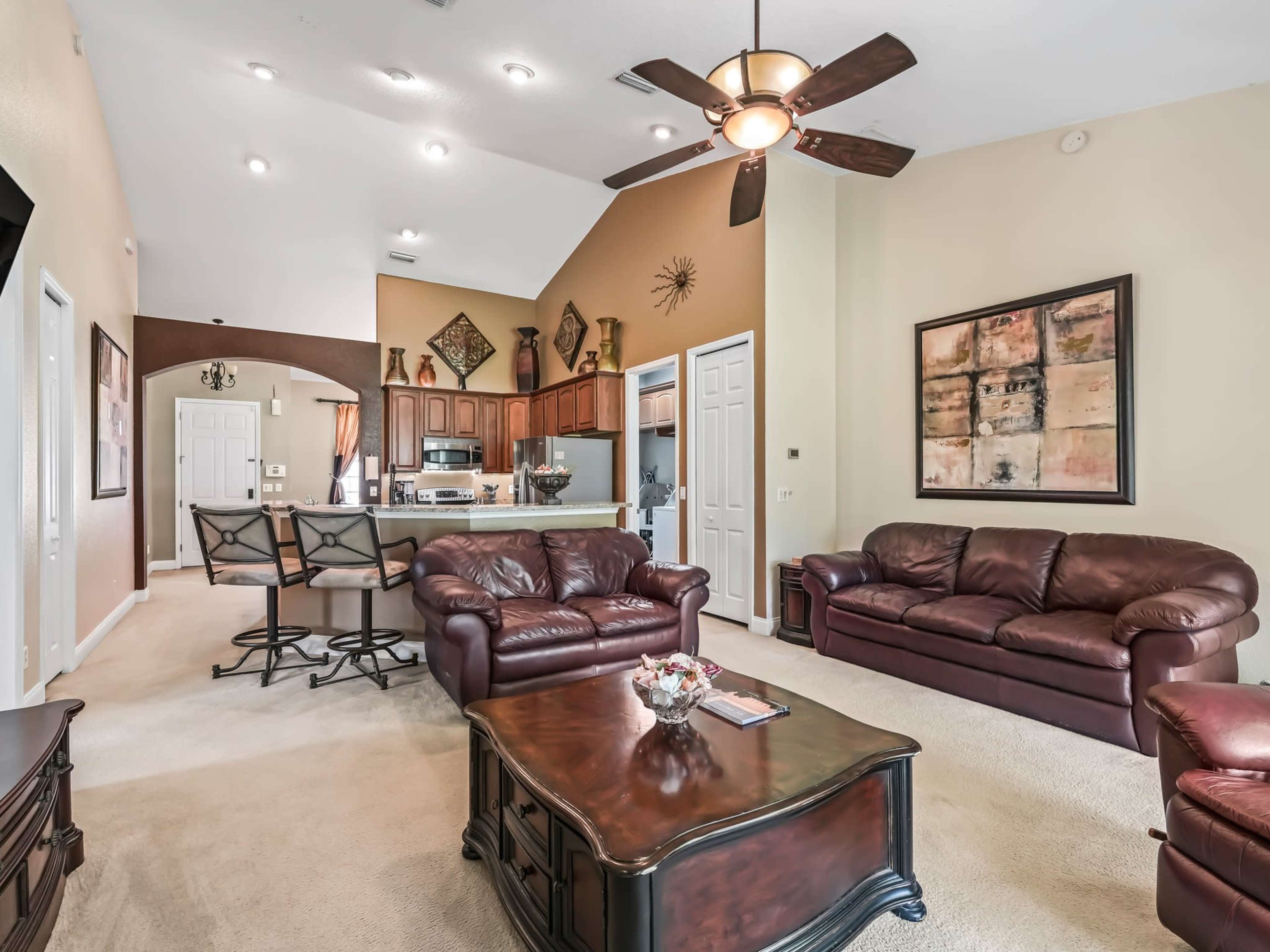 A spacious living room featuring two brown leather couches, a coffee table, and an open kitchen area in the background with wooden cabinets.