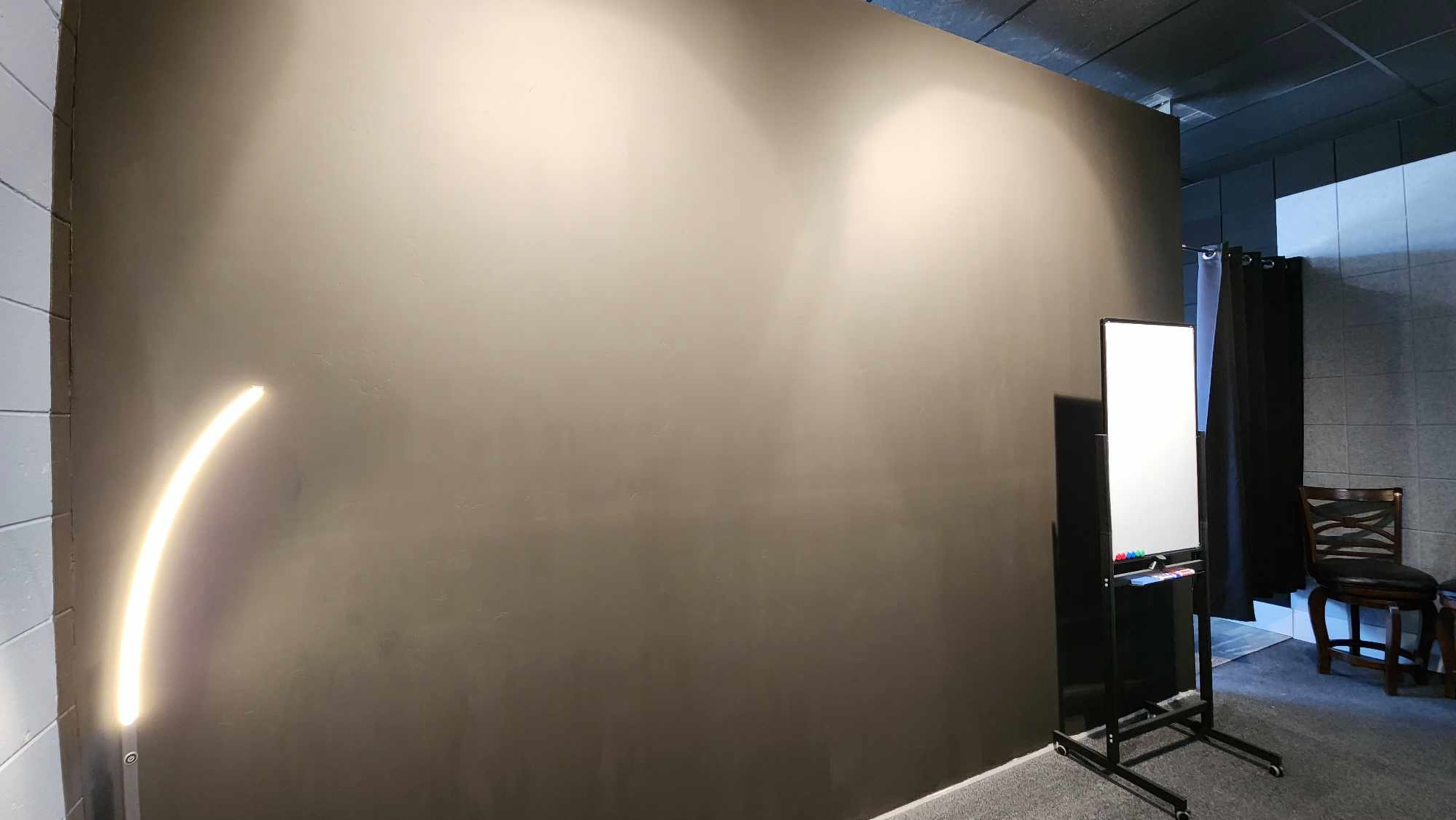 A blank, dark wall with a stand holding a mirror and a chair in a dimly lit room.