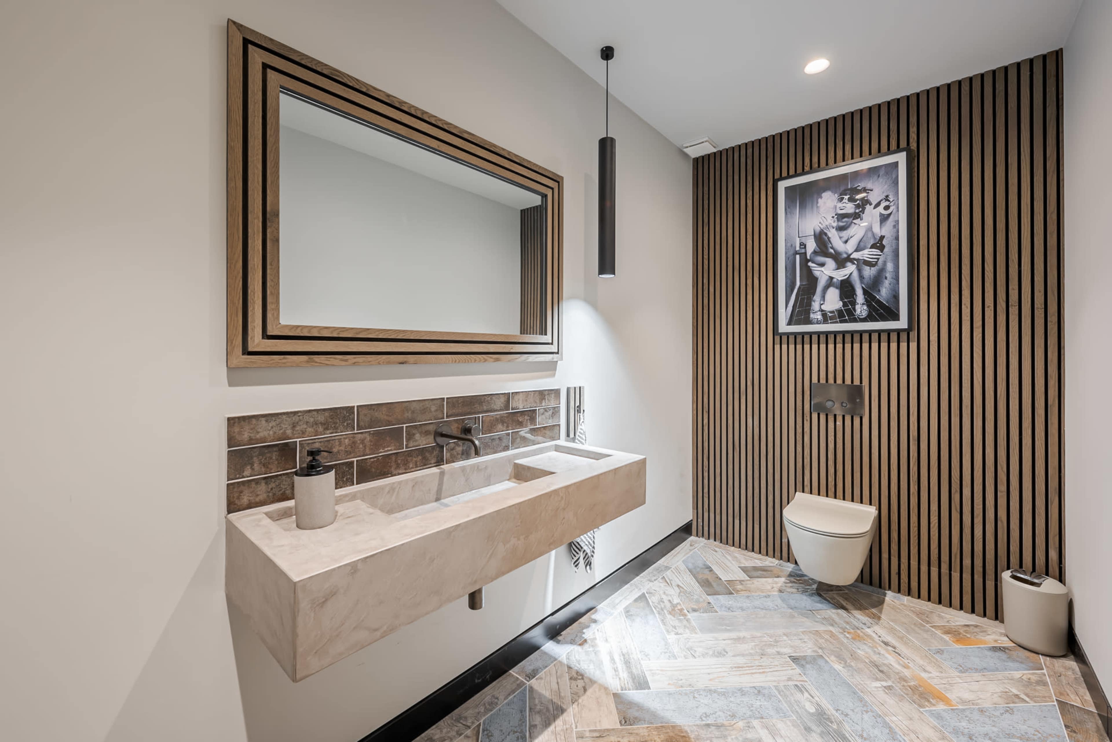 A modern bathroom featuring a rectangular stone sink, a large mirror with a wooden frame, and a wall-mounted toilet against a backdrop of vertical wooden paneling.