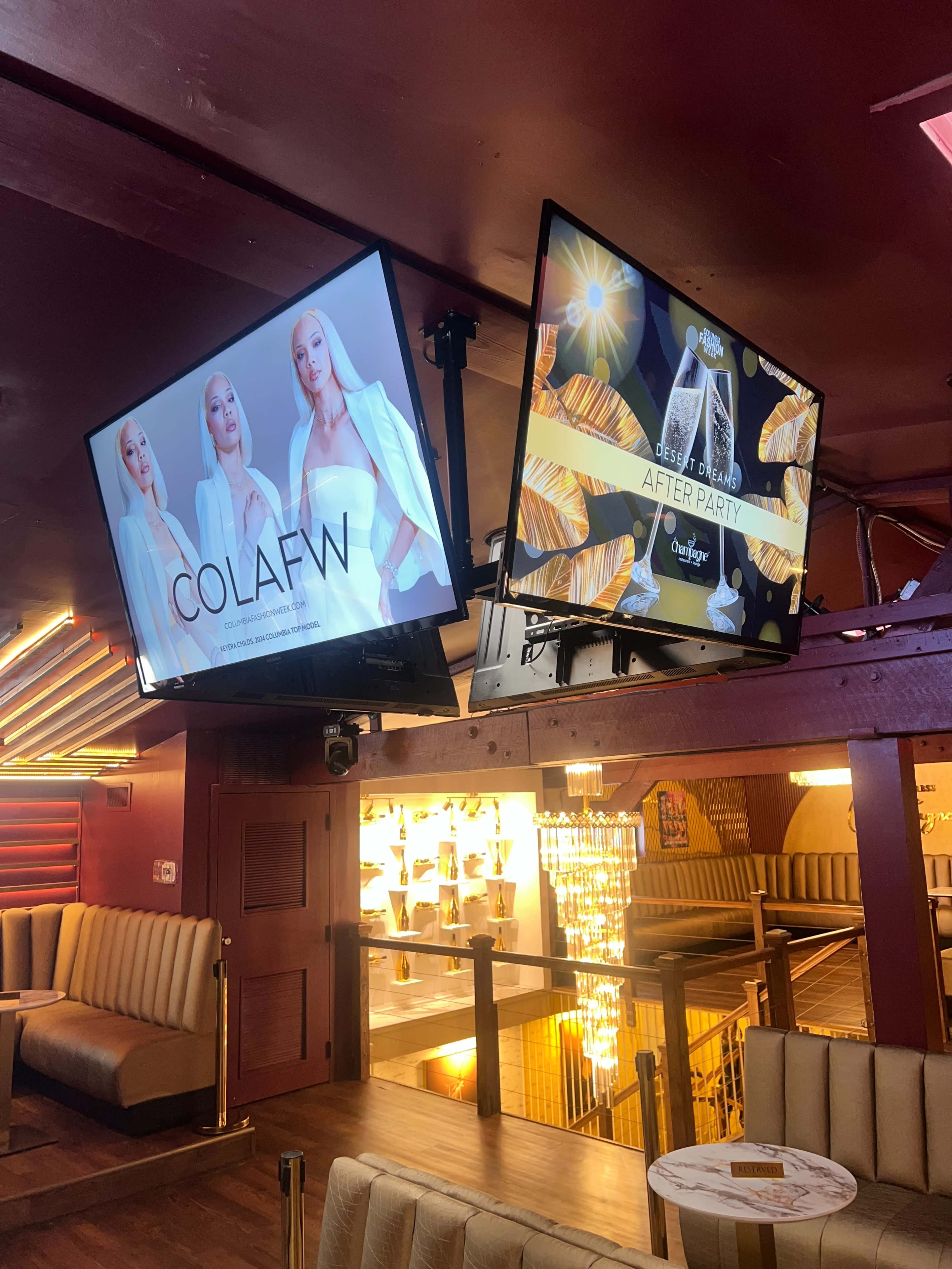 The image shows two screens mounted on a wooden wall, one displaying a model promoting a brand called "COLAFWN" and the other advertising an "AFTER PARTY" event.