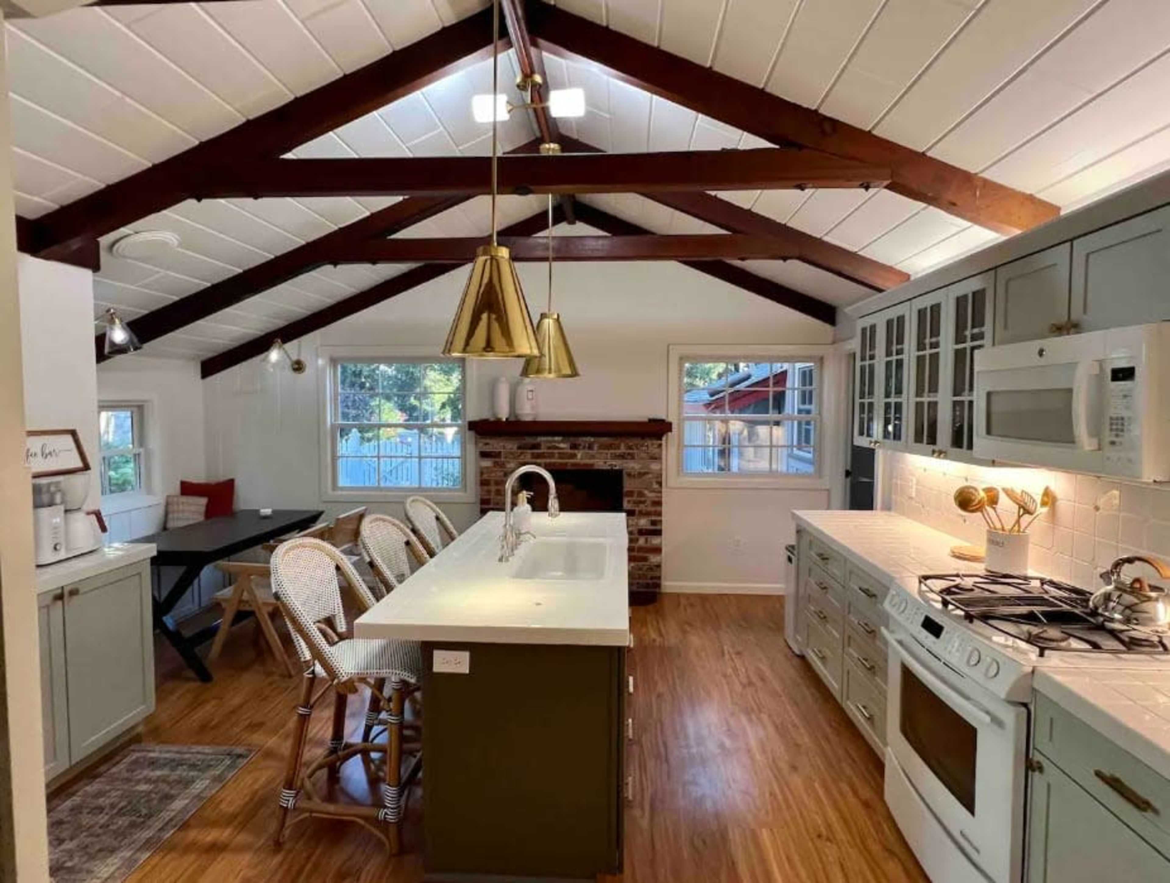 A kitchen with a high ceiling, wooden beams, a central island with bar seating, and a brick fireplace.
