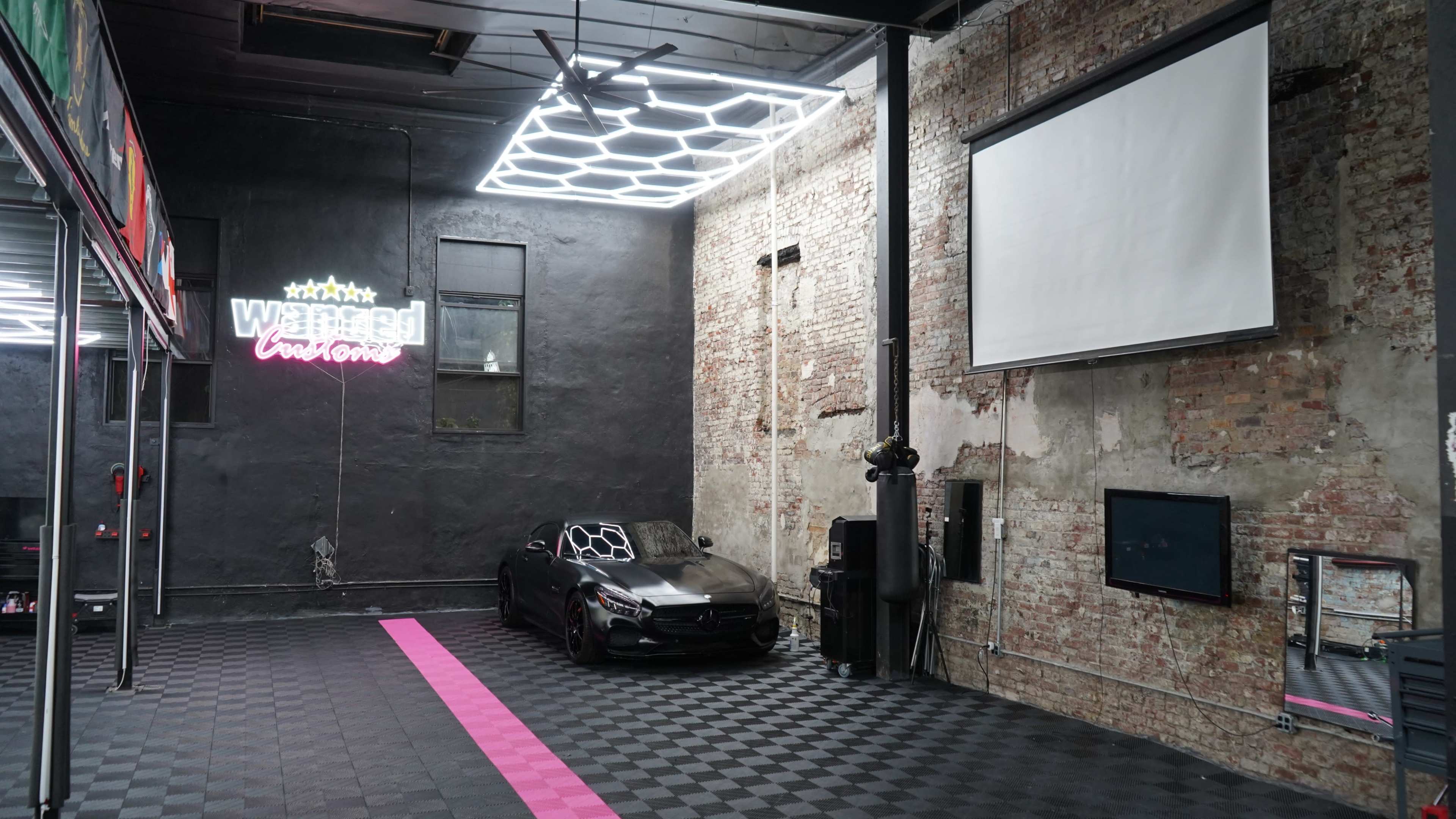 The image shows a spacious interior with a blackened brick wall, a sleek black car parked on a checkered floor, and a neon sign that reads "Wasted Customs."