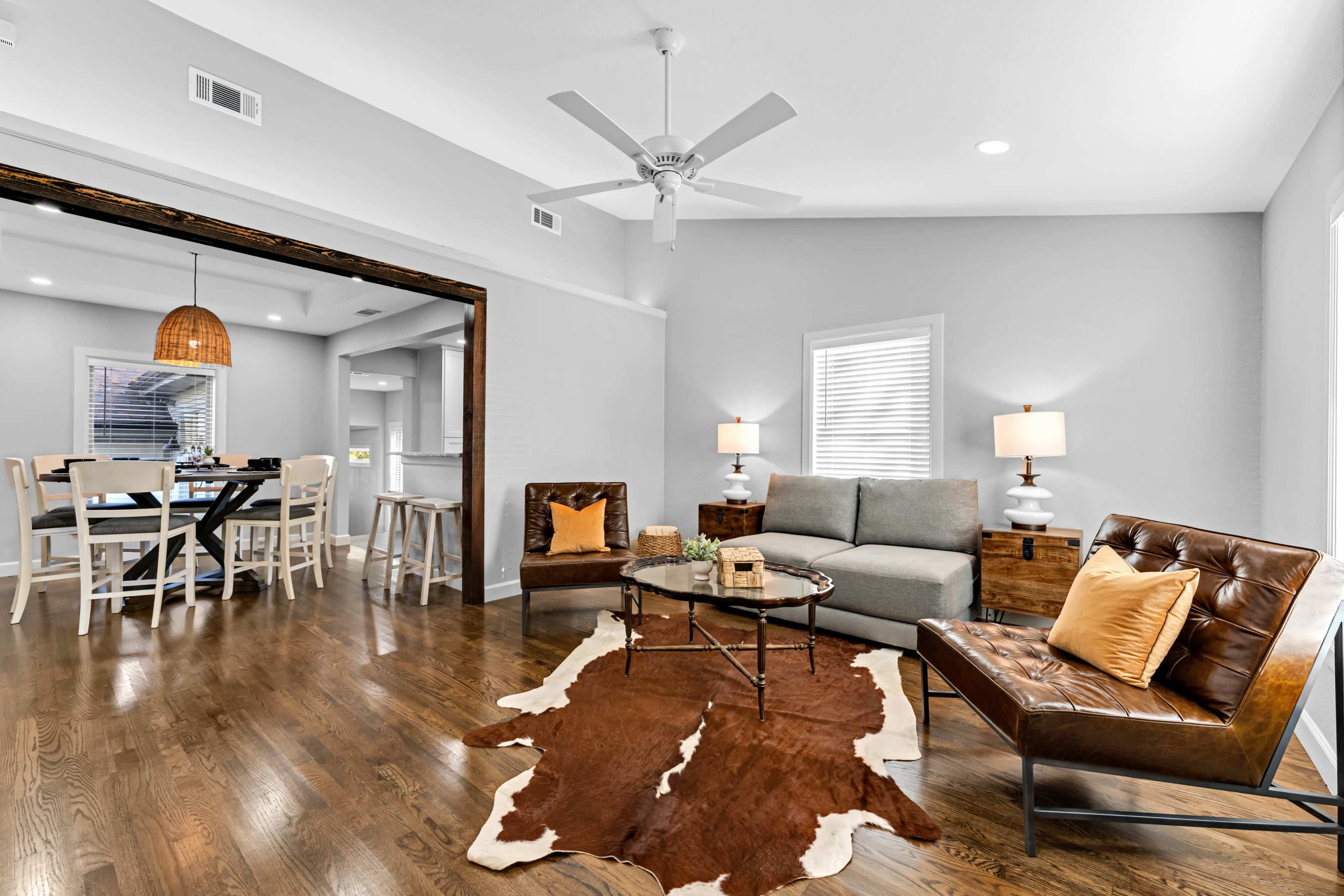 A modern living room with a gray sofa, two brown chairs, and a wooden coffee table arranged on hardwood flooring, with a dining area in the background.