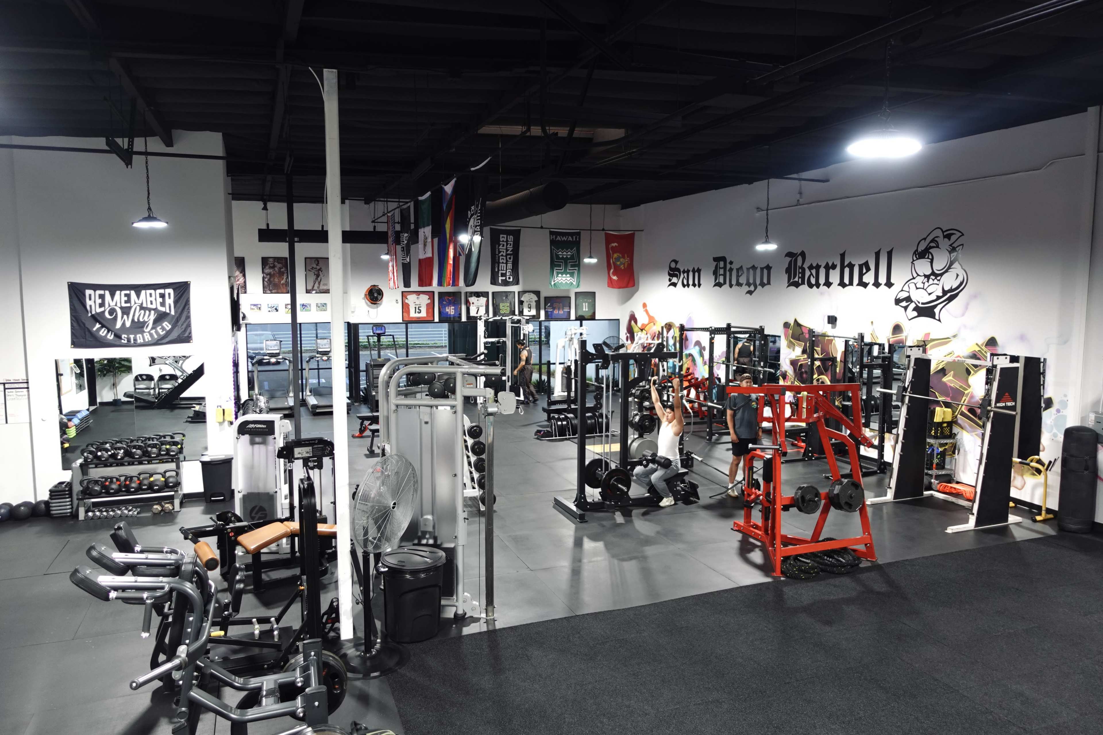 The gym features various workout equipment, including weightlifting machines and free weights, with banners and flags hanging on the walls.
