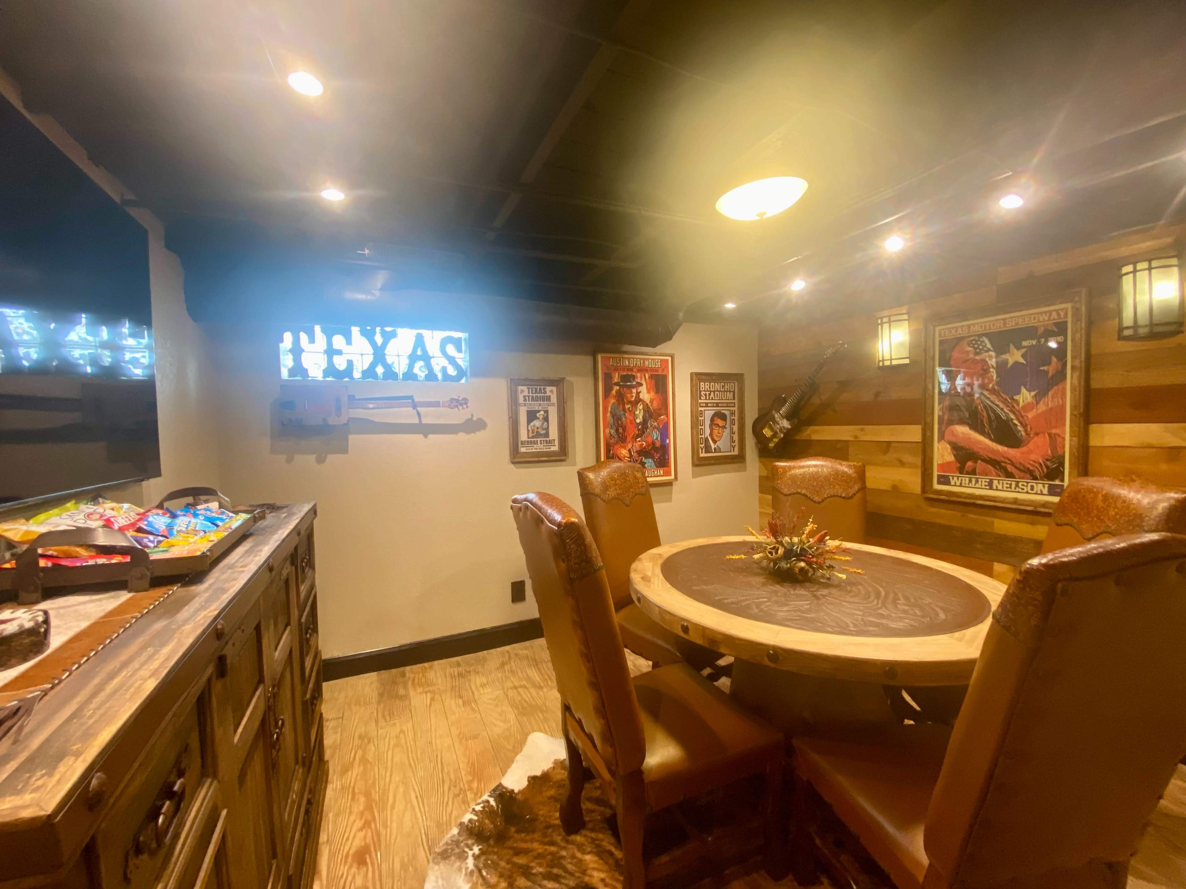 A rustic dining area with a circular wooden table surrounded by leather chairs, adorned with framed posters and decorative items on the walls.