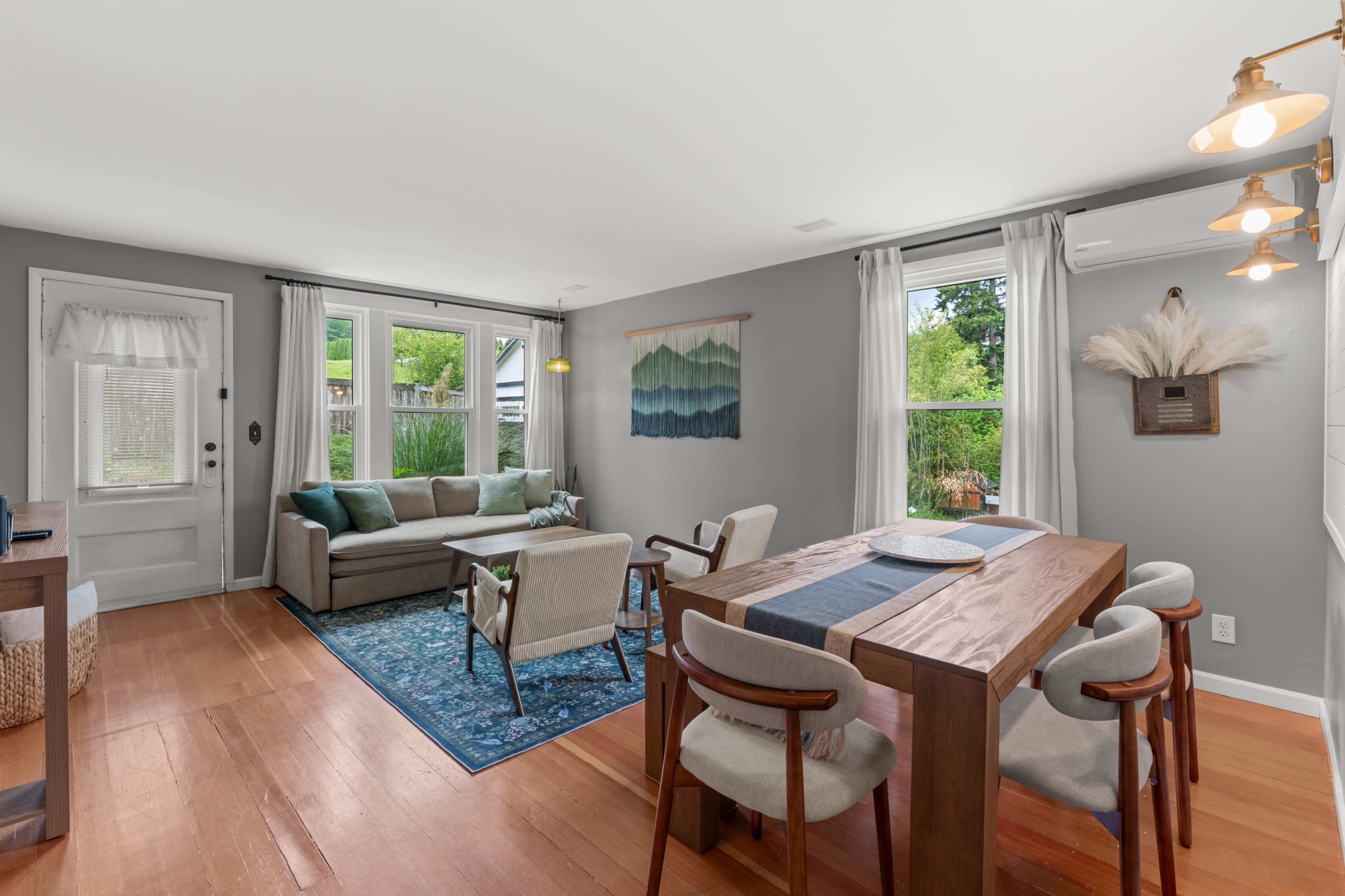 The living area features a sofa, dining table, and large windows that provide ample natural light.