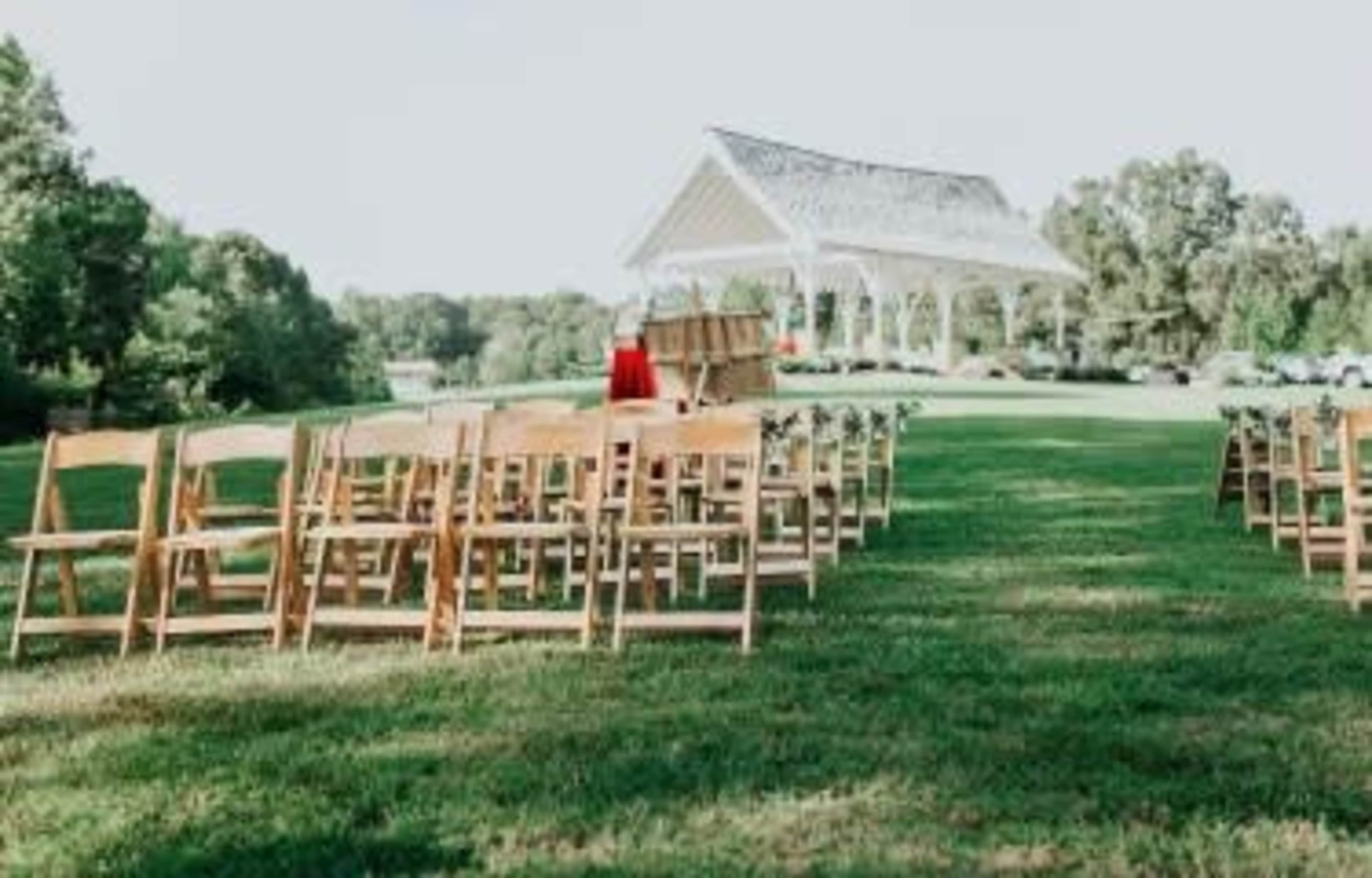 A set of wooden chairs is arranged in rows facing a decorated gazebo on a grassy field.