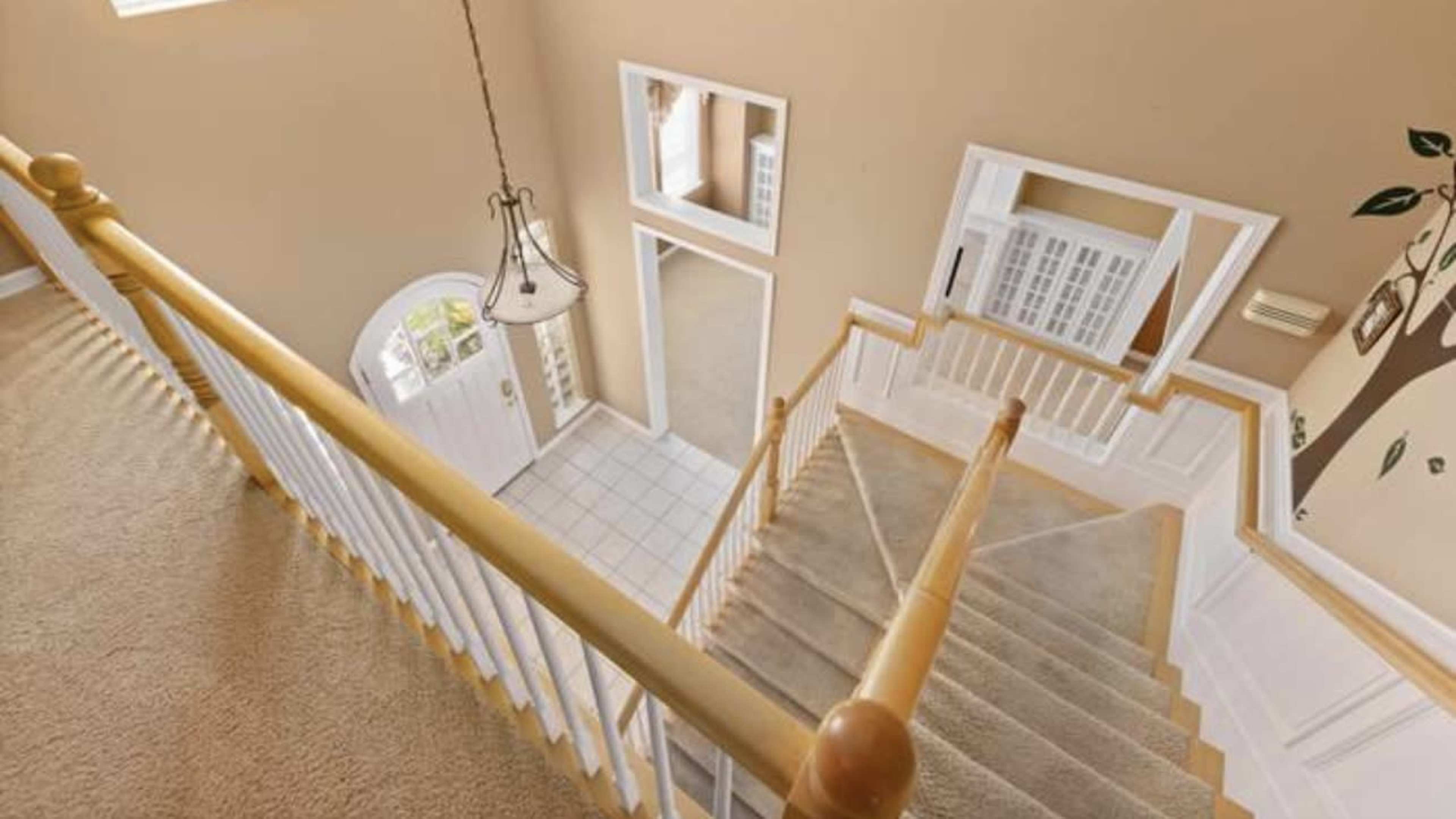 An interior view of a staircase leading down to an entrance area, with a light fixture and wall decorations visible.