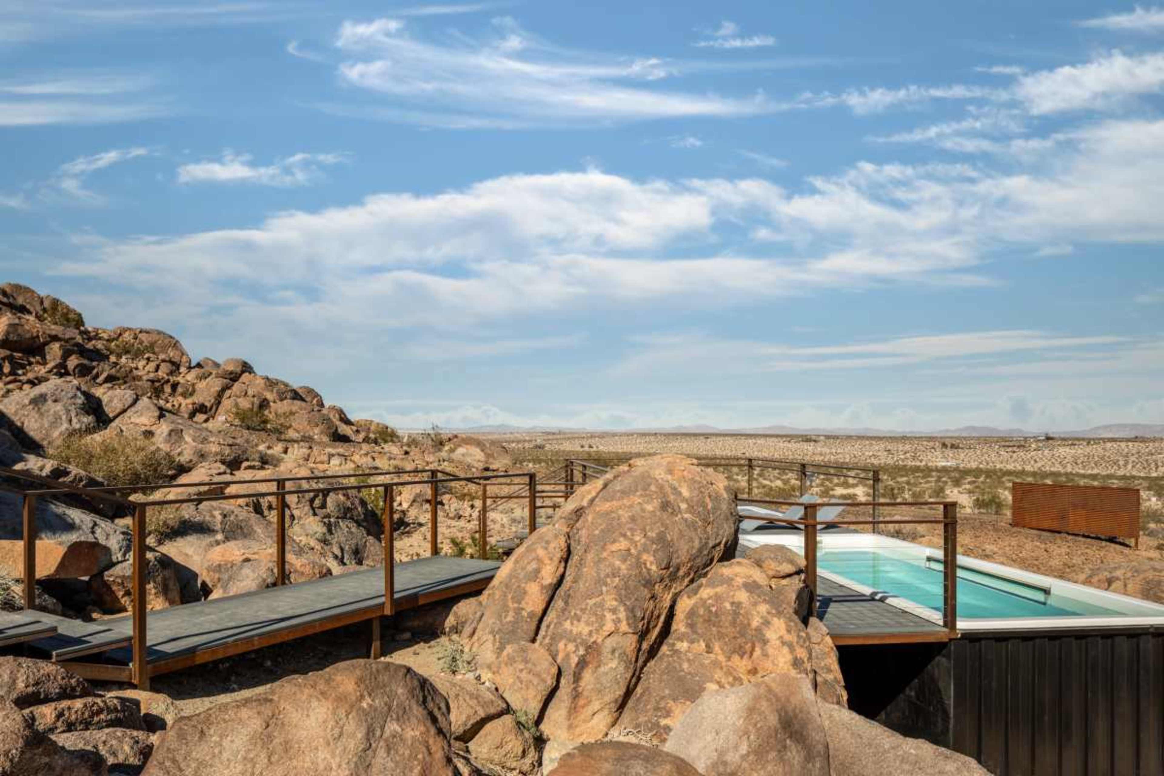 A modern pool set amidst large boulders in a desert landscape under a blue sky.