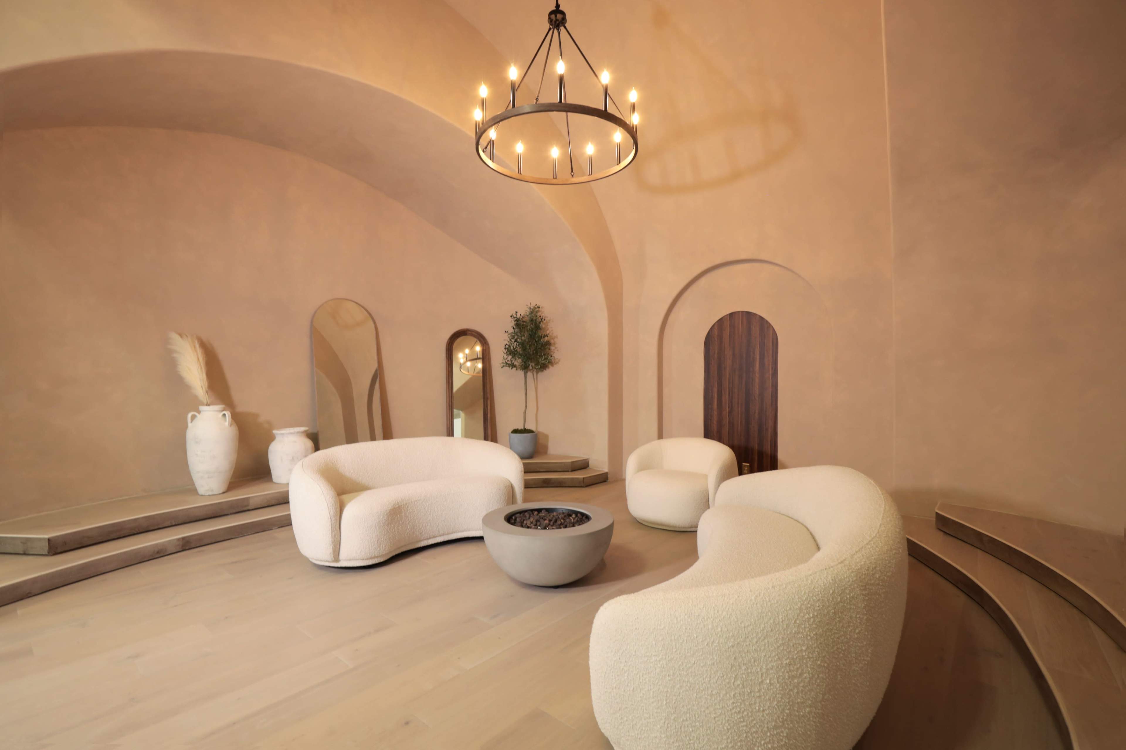 A modern interior space with curved seating, a round coffee table, and simple decor elements under a circular chandelier.