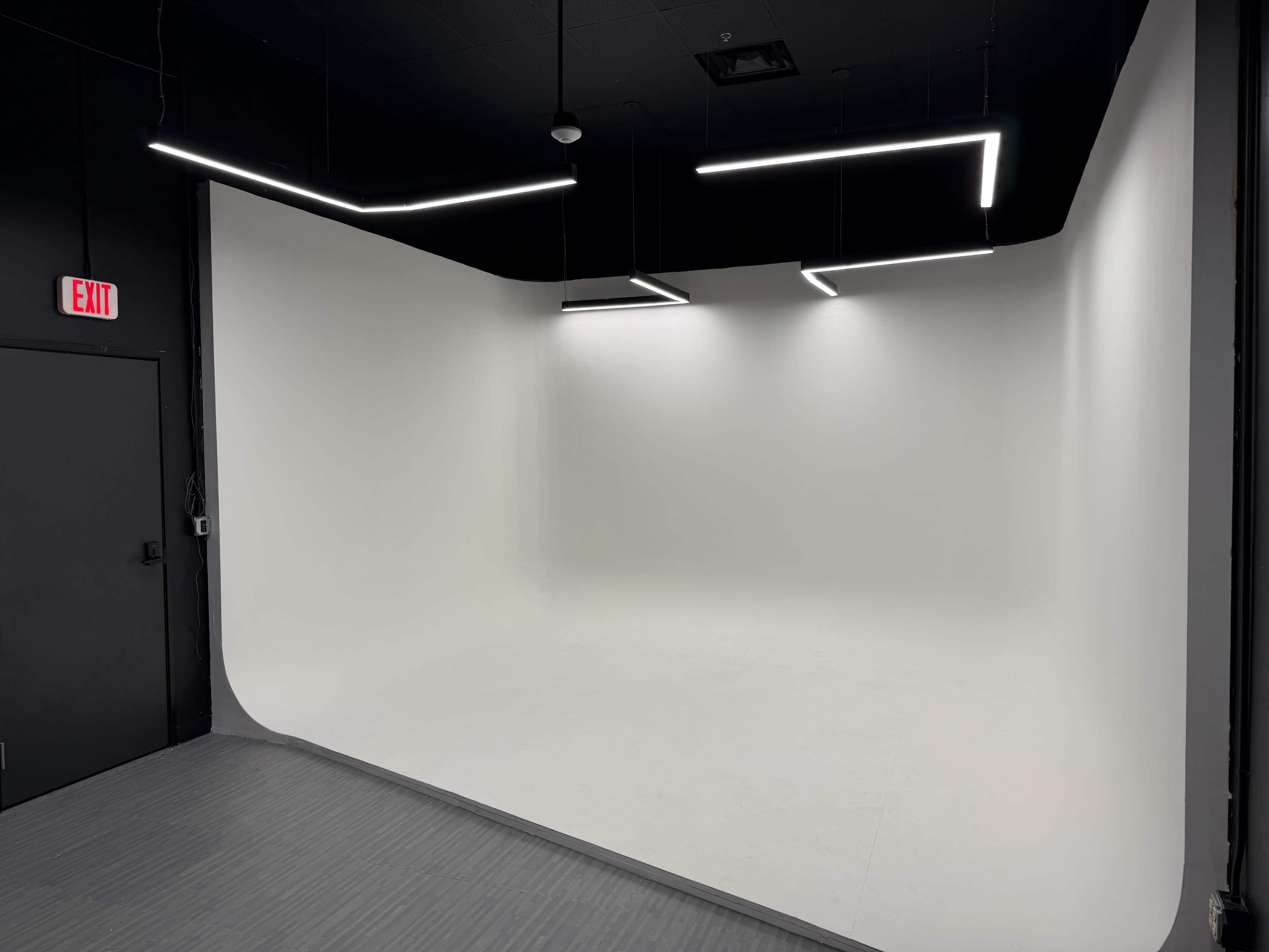 The image shows a minimalist studio space with a curved white backdrop and modern ceiling lights.