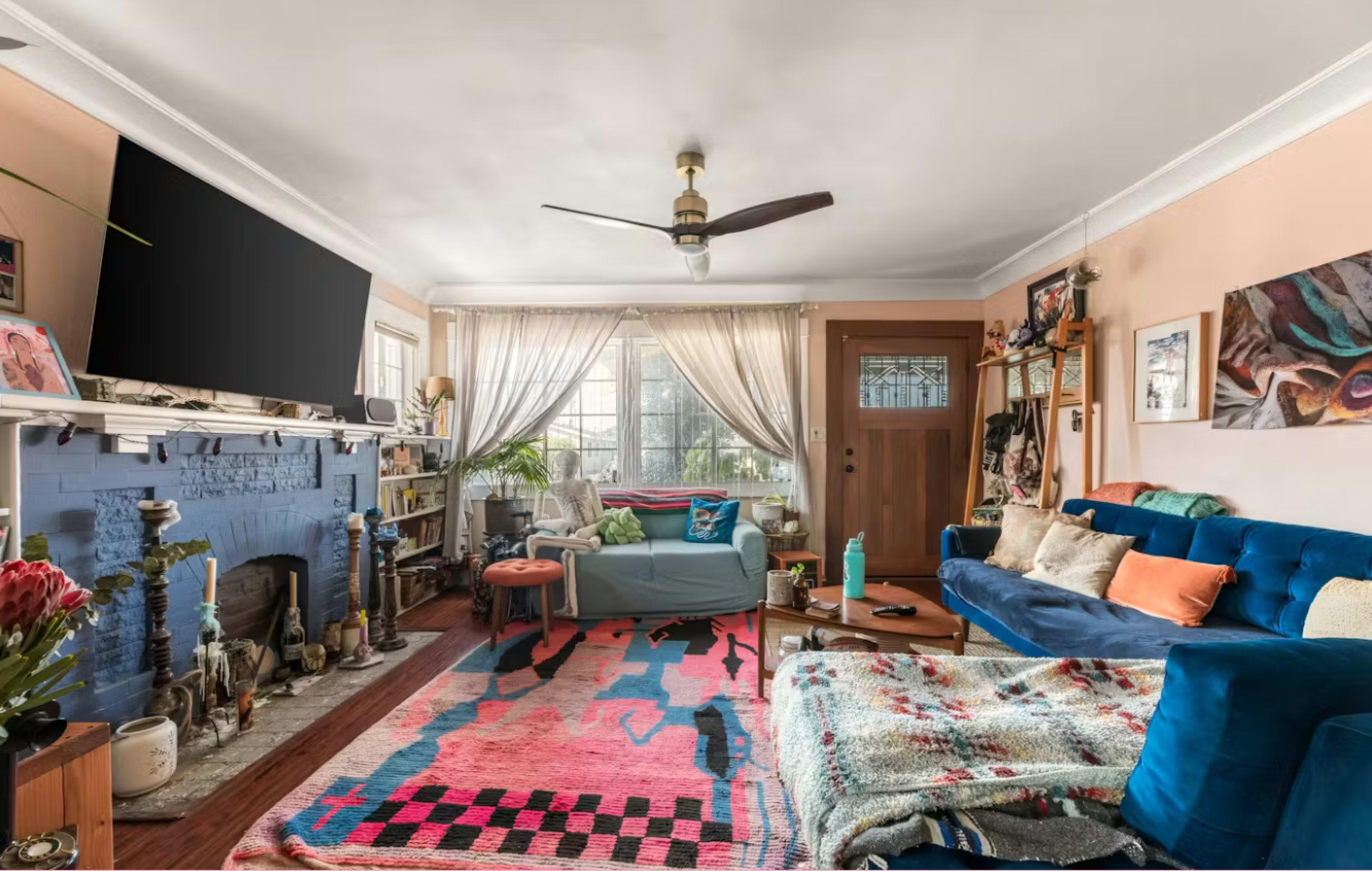 The living room features a blue couch, a pink and black patterned rug, and a decorative fireplace with a large television mounted above it.