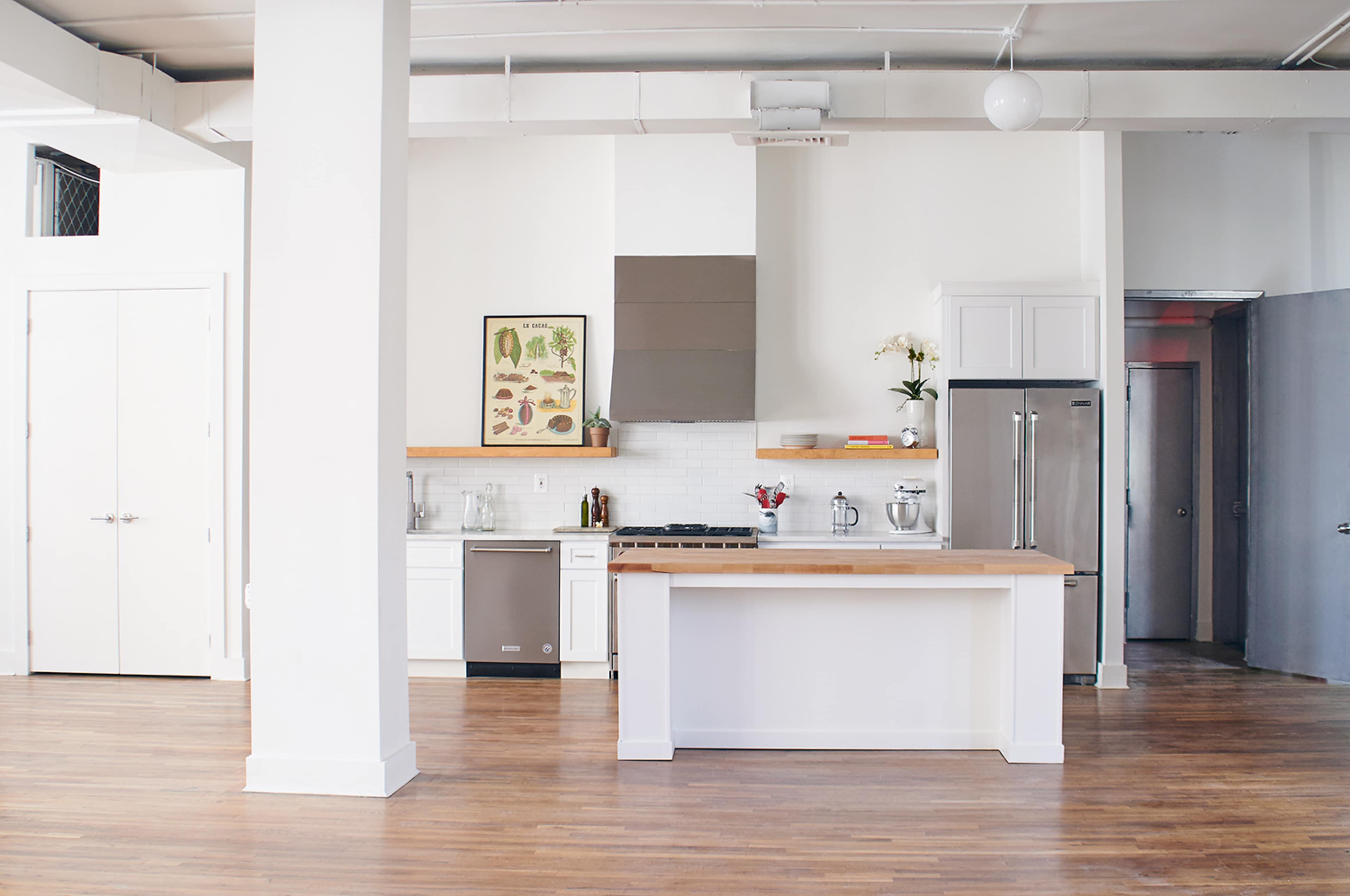 A modern kitchen with a central island, stainless steel appliances, and white cabinetry in a spacious room with hardwood flooring.