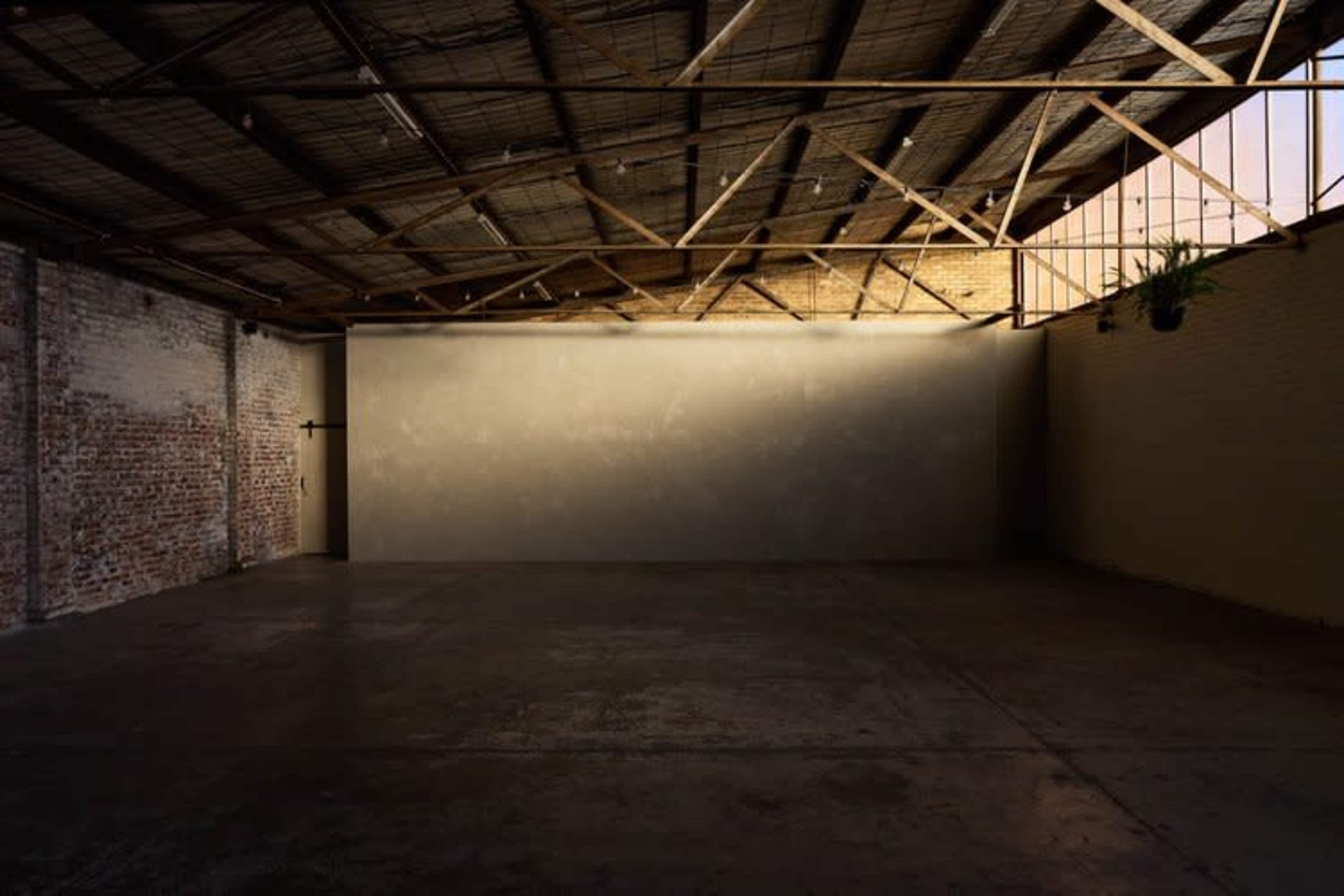 A spacious, empty room with a concrete floor and exposed wooden beams overhead.