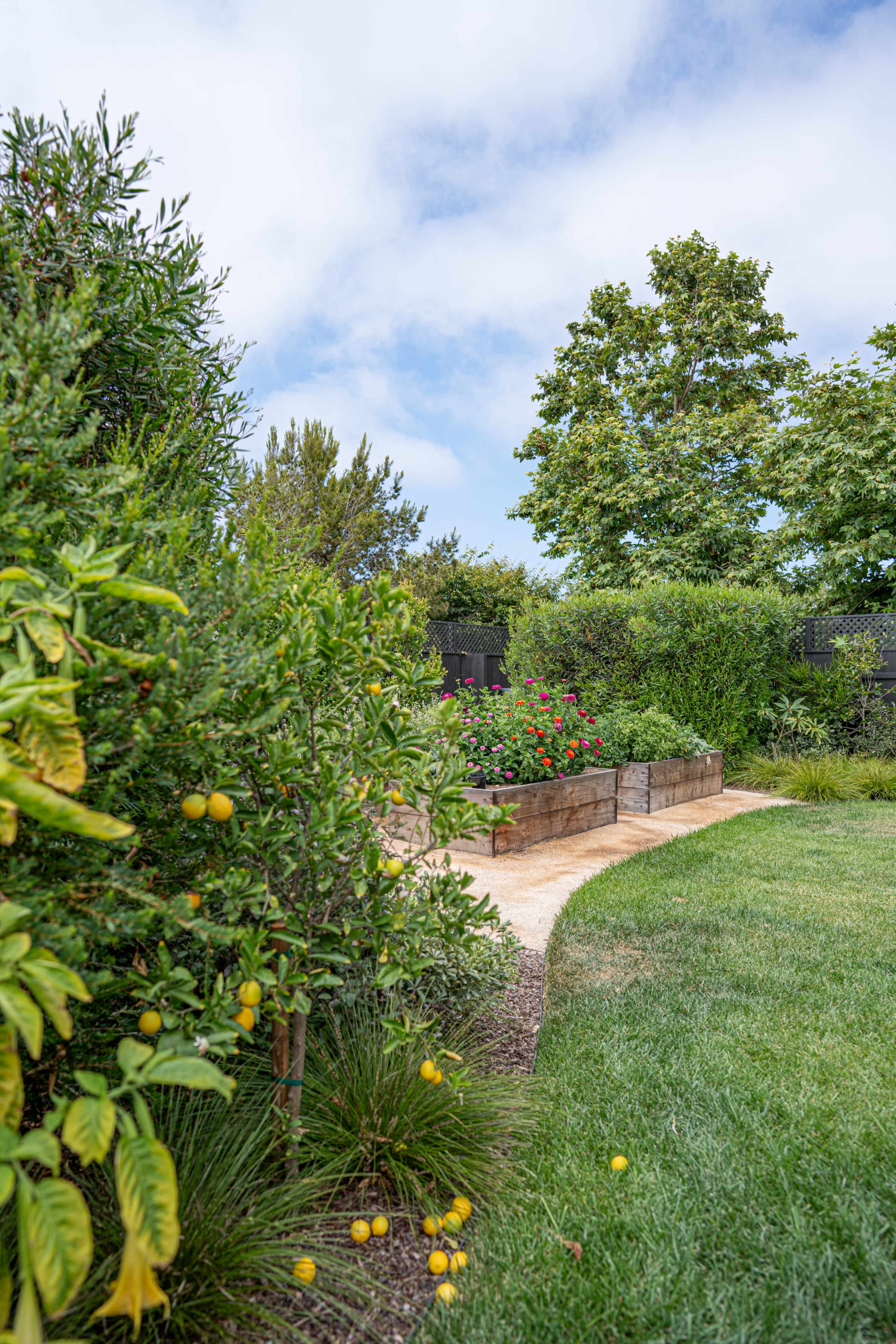 A well-maintained garden path leads through lush greenery and flowering plants, with raised garden beds visible in the background.