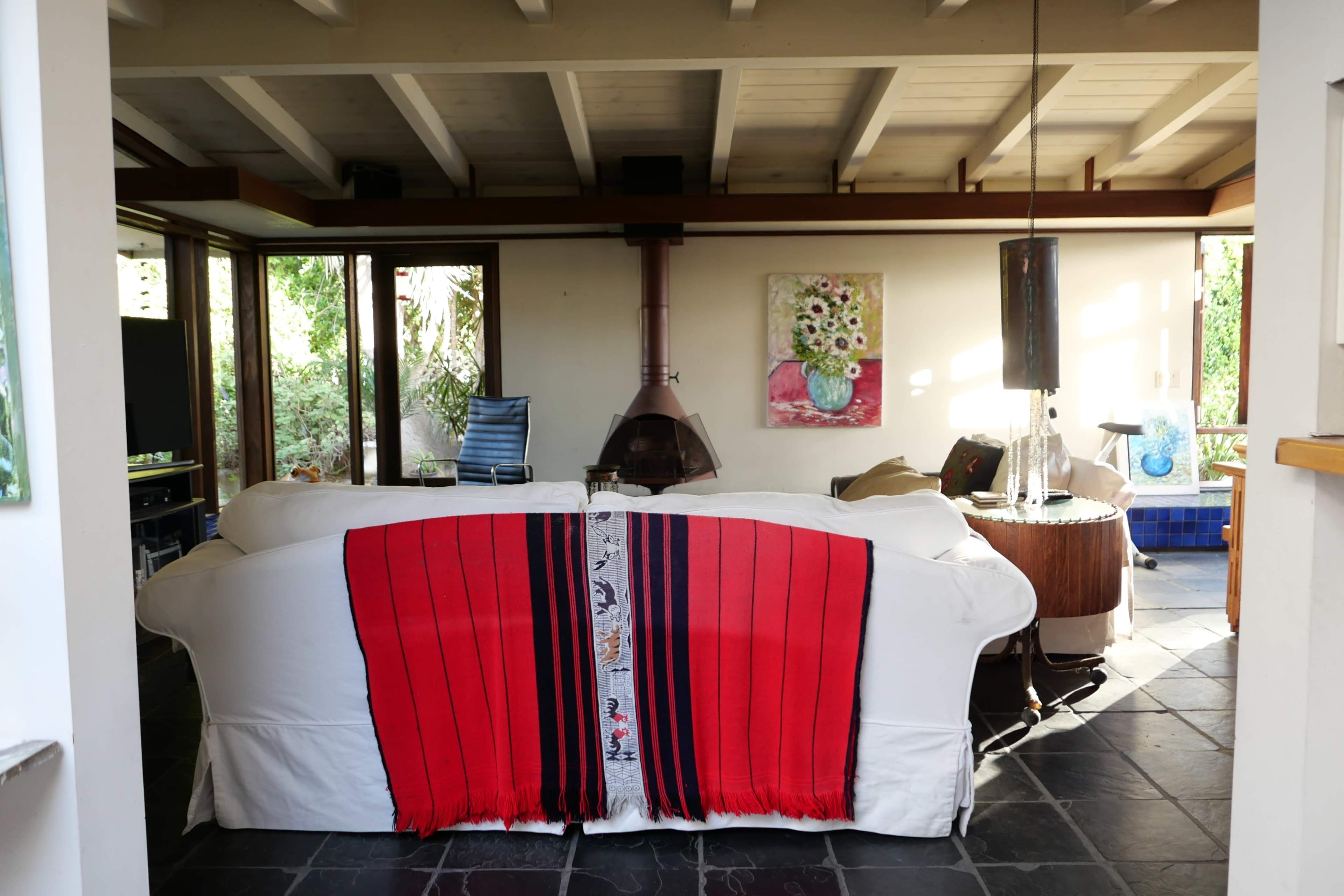 A living room with a white sofa draped with a red and blue blanket, a wooden coffee table, and a fireplace in the background.