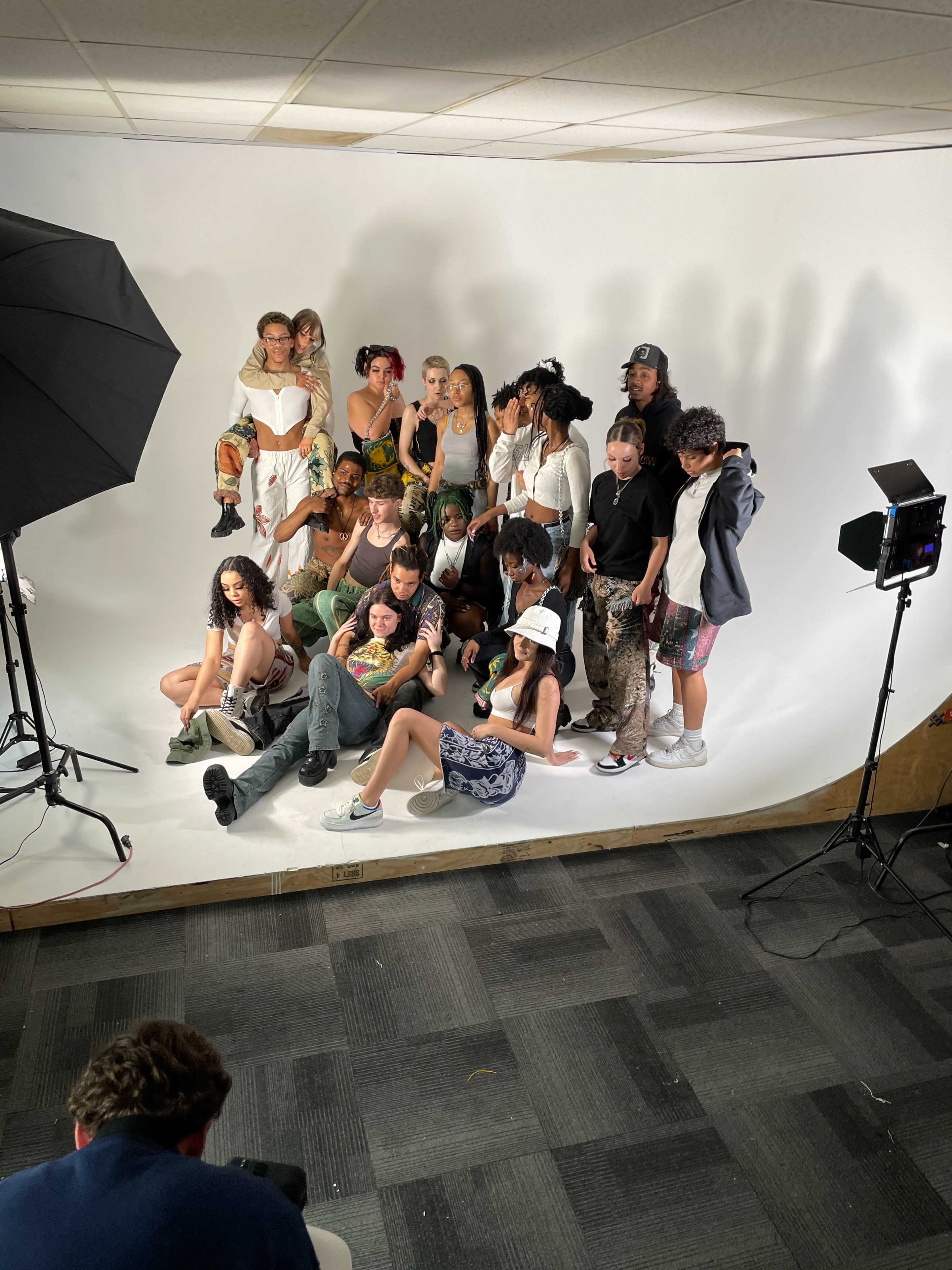 A group of diverse models poses together for a photoshoot in a studio with soft lighting and a plain backdrop.