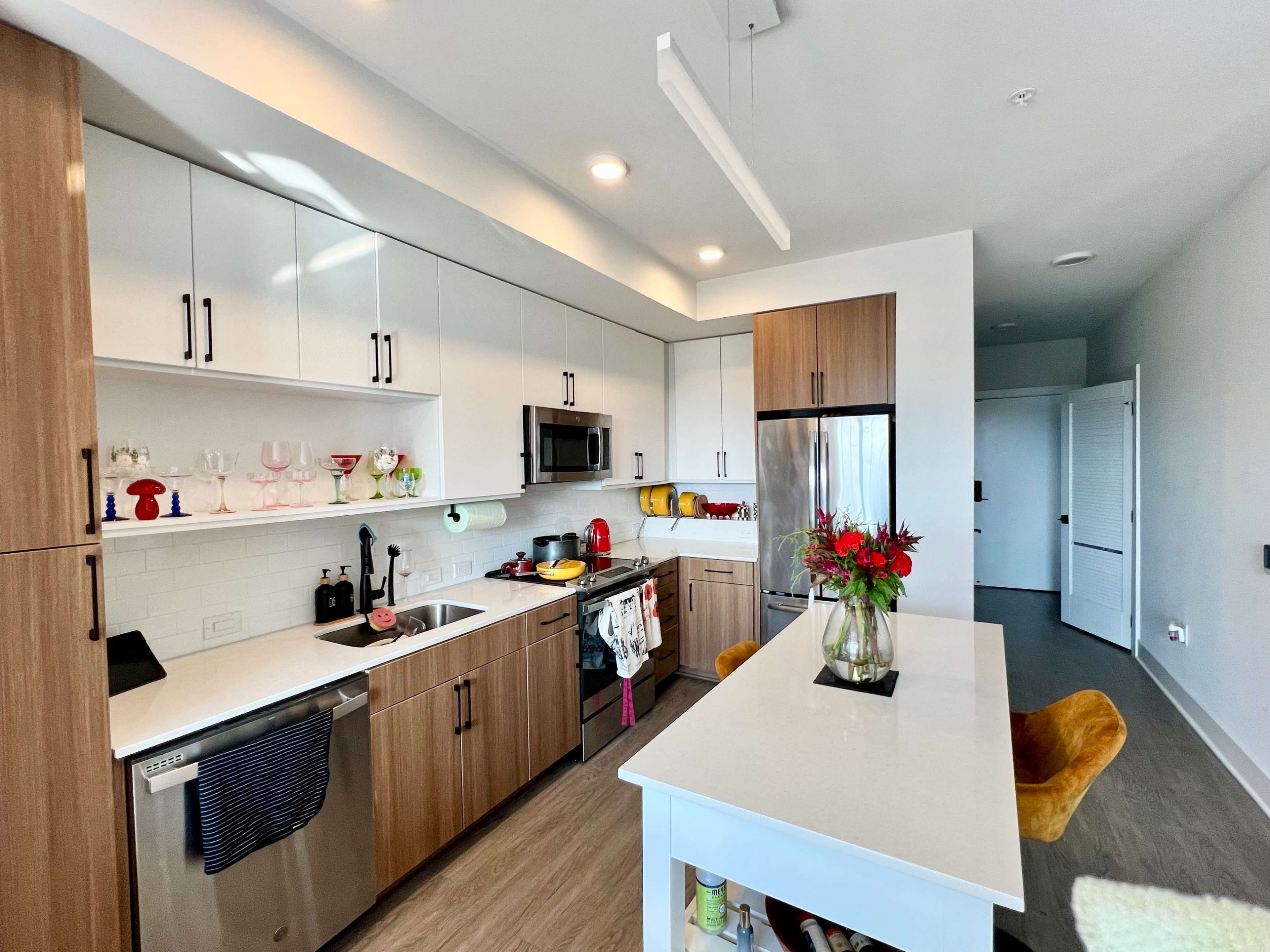 A modern kitchen features wooden cabinetry, stainless steel appliances, and a central island with a flower vase.