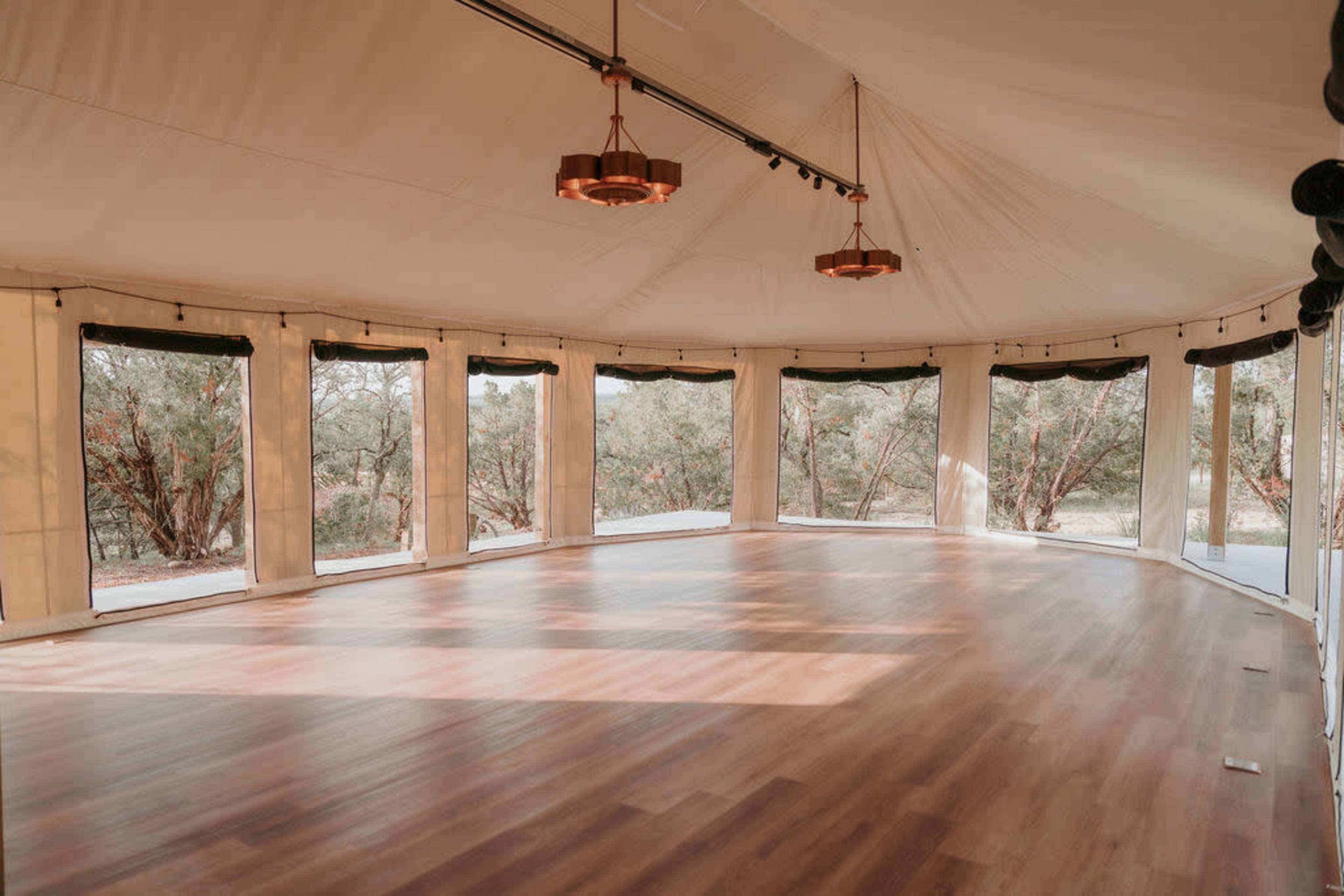 A spacious, illuminated interior of a tent with large windows and wooden flooring.