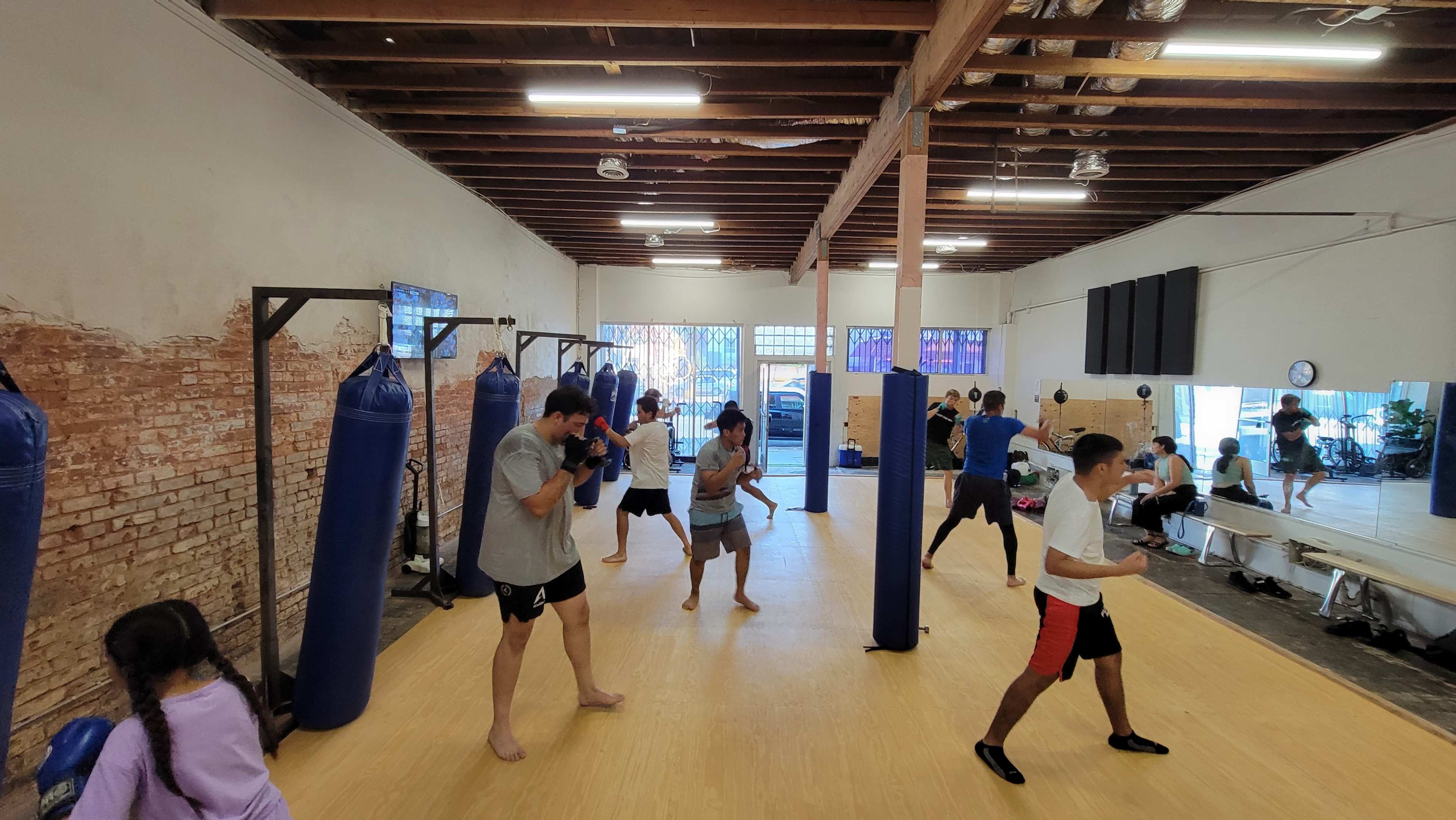 A group of individuals trains in a boxing gym with heavy punching bags and a wooden floor.