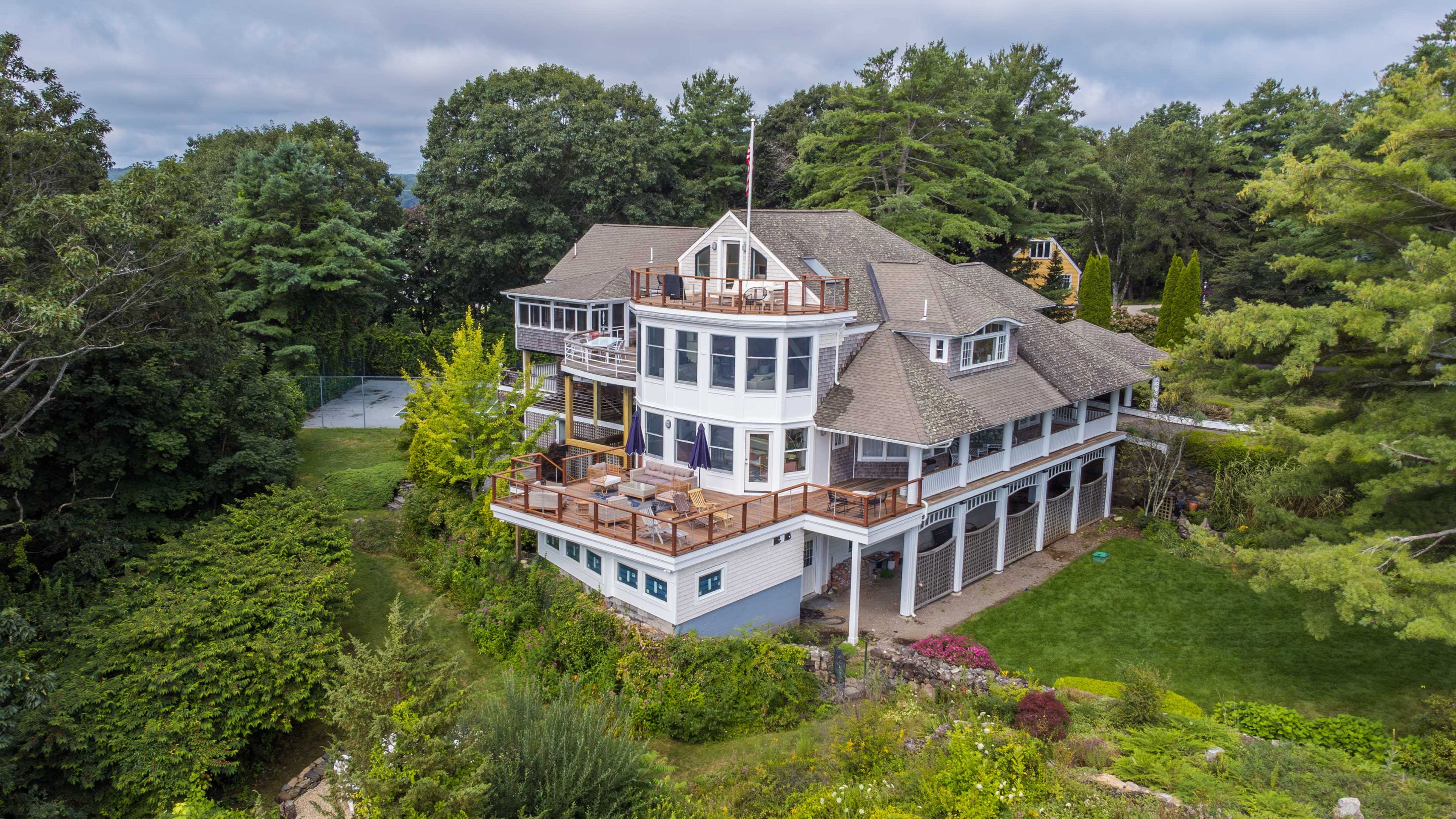 A large, multi-level house with numerous decks and an expansive yard surrounded by trees.