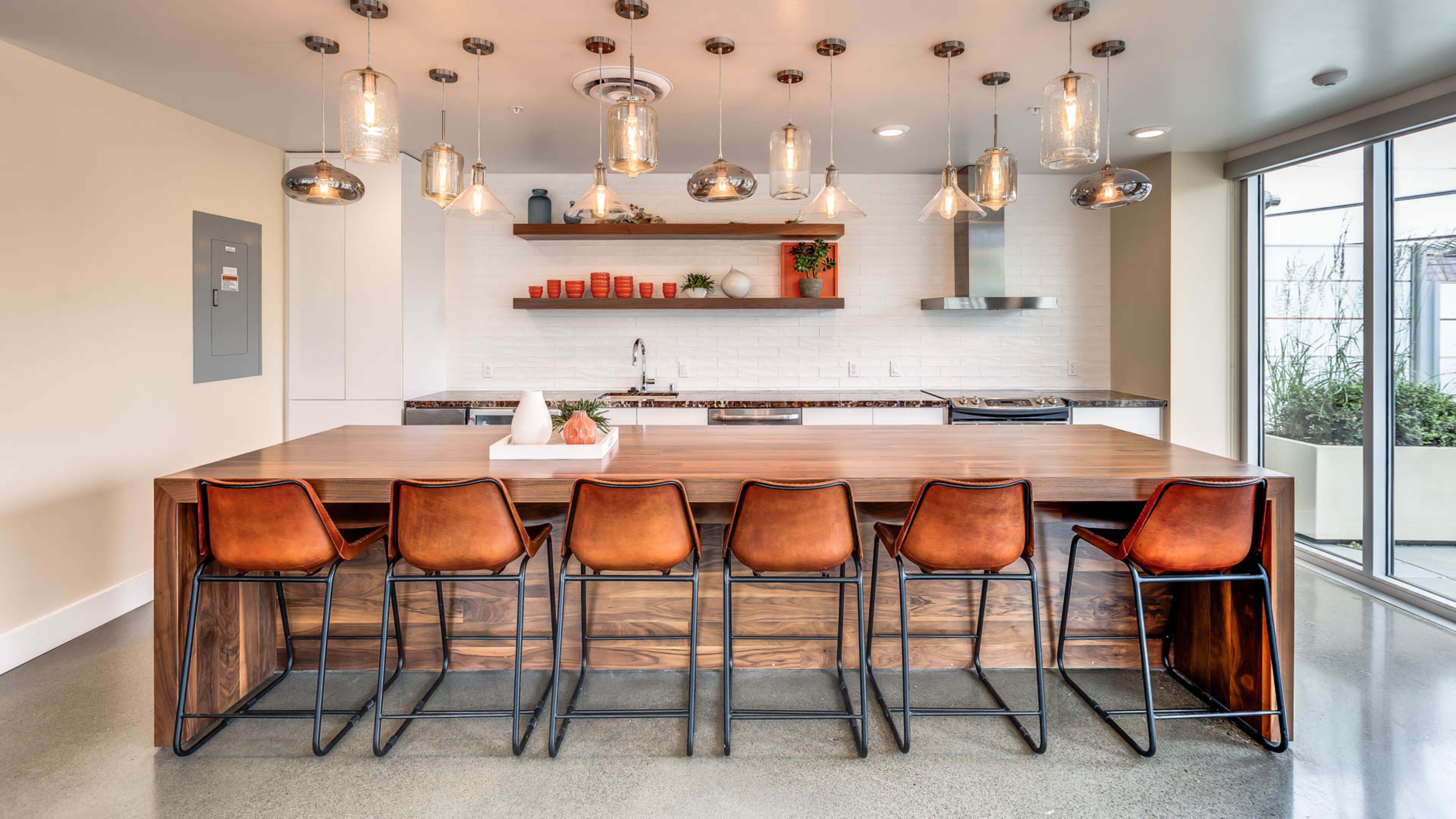 A modern kitchen features a large wooden island with metal bar stools, pendant lighting, and a minimalist design.