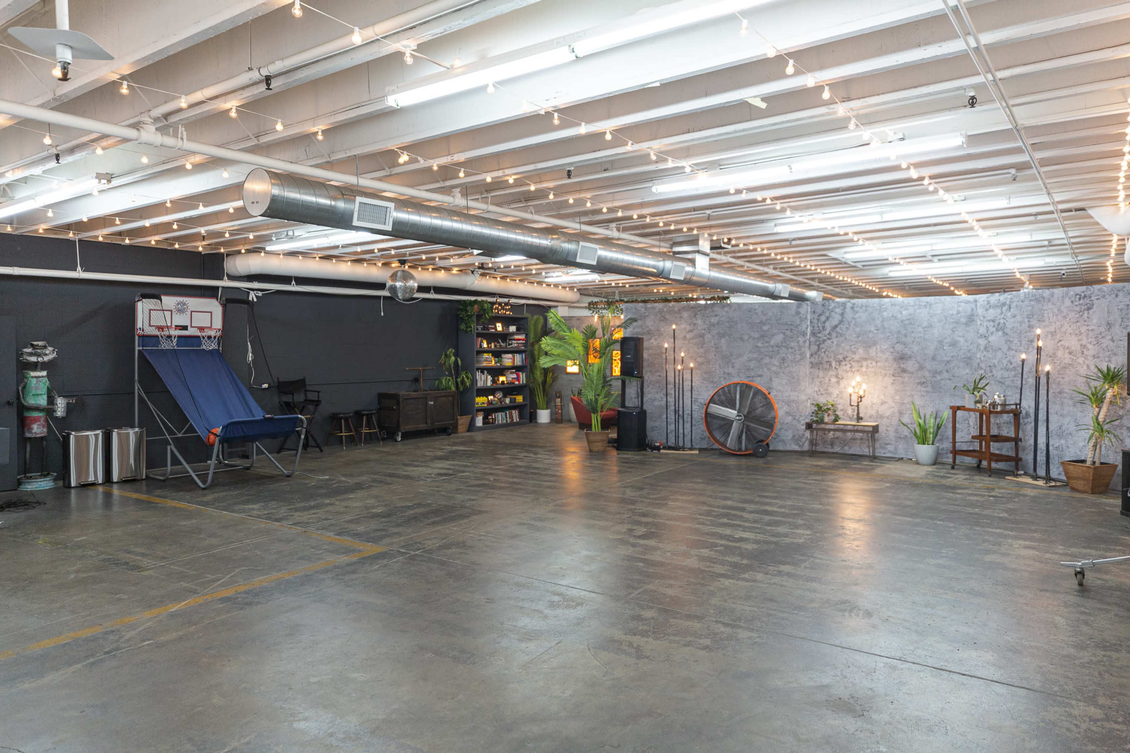 A spacious, well-lit commercial area with modern lighting, concrete floors, and a few decorative elements like plants, shelves, and seating.