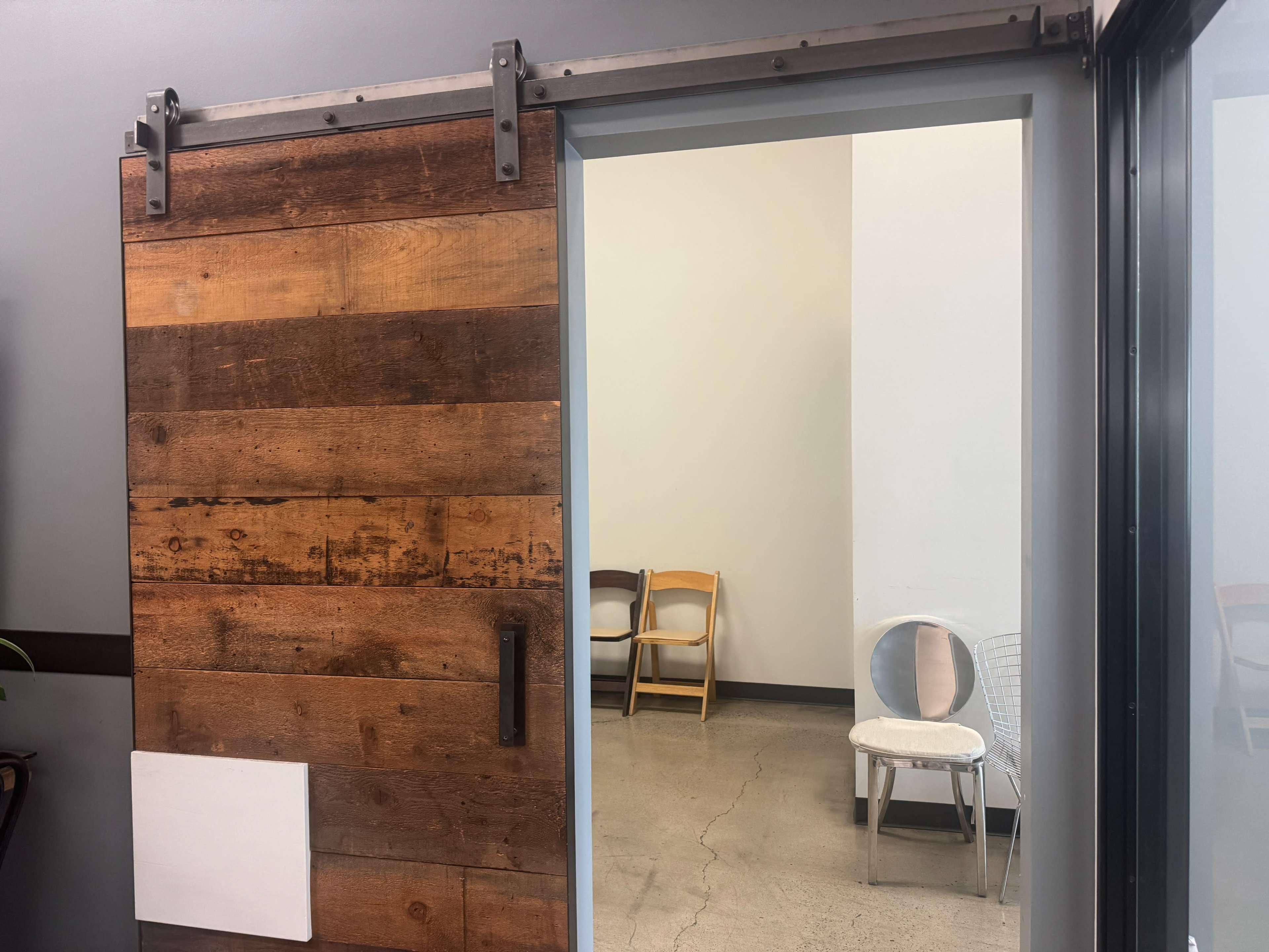 A wooden sliding door partially opens to reveal a minimalistic room with folding chairs and a light-colored wall.