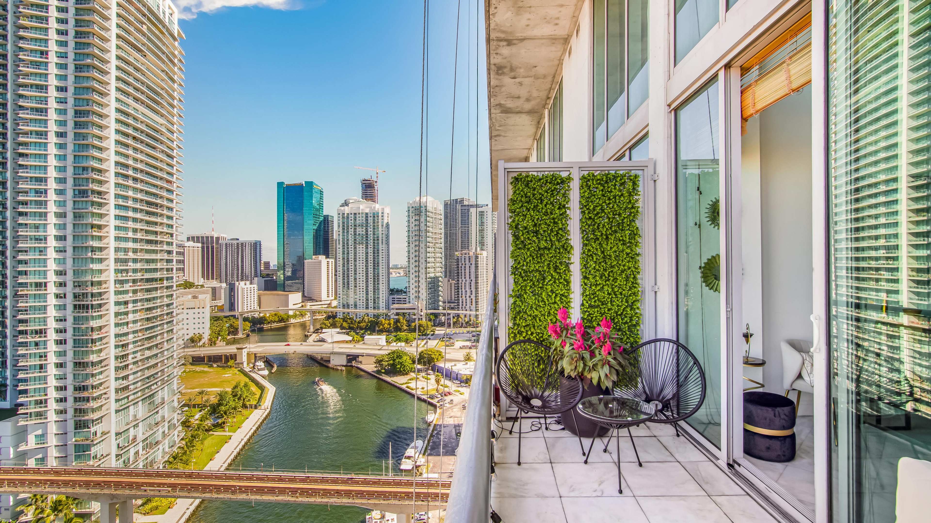 A balcony with potted plants overlooks a river and city skyline featuring modern skyscrapers.