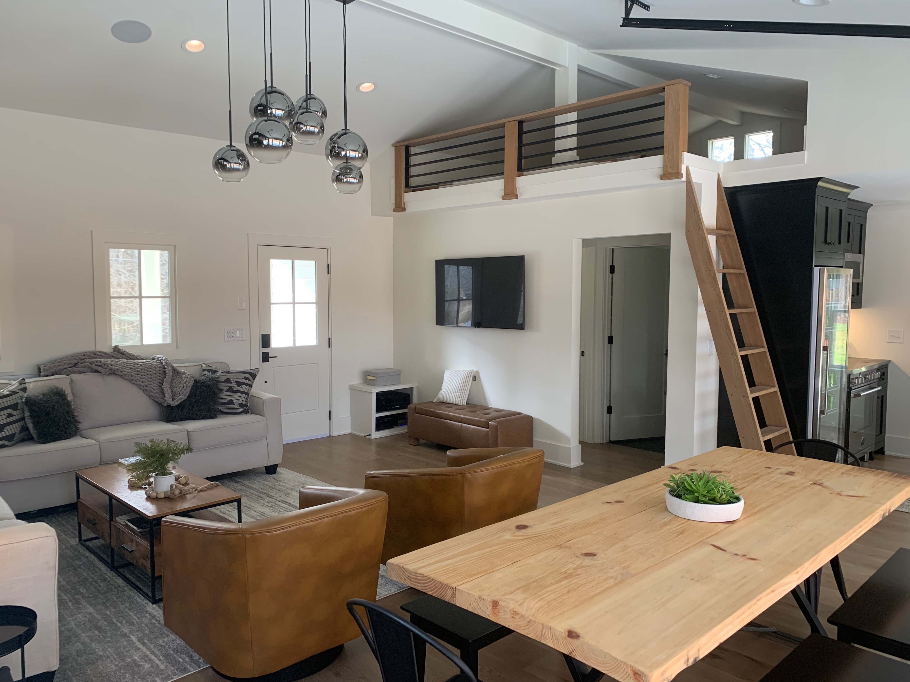 A modern living space with a seating area, a wooden dining table, and a ladder leading to a loft.