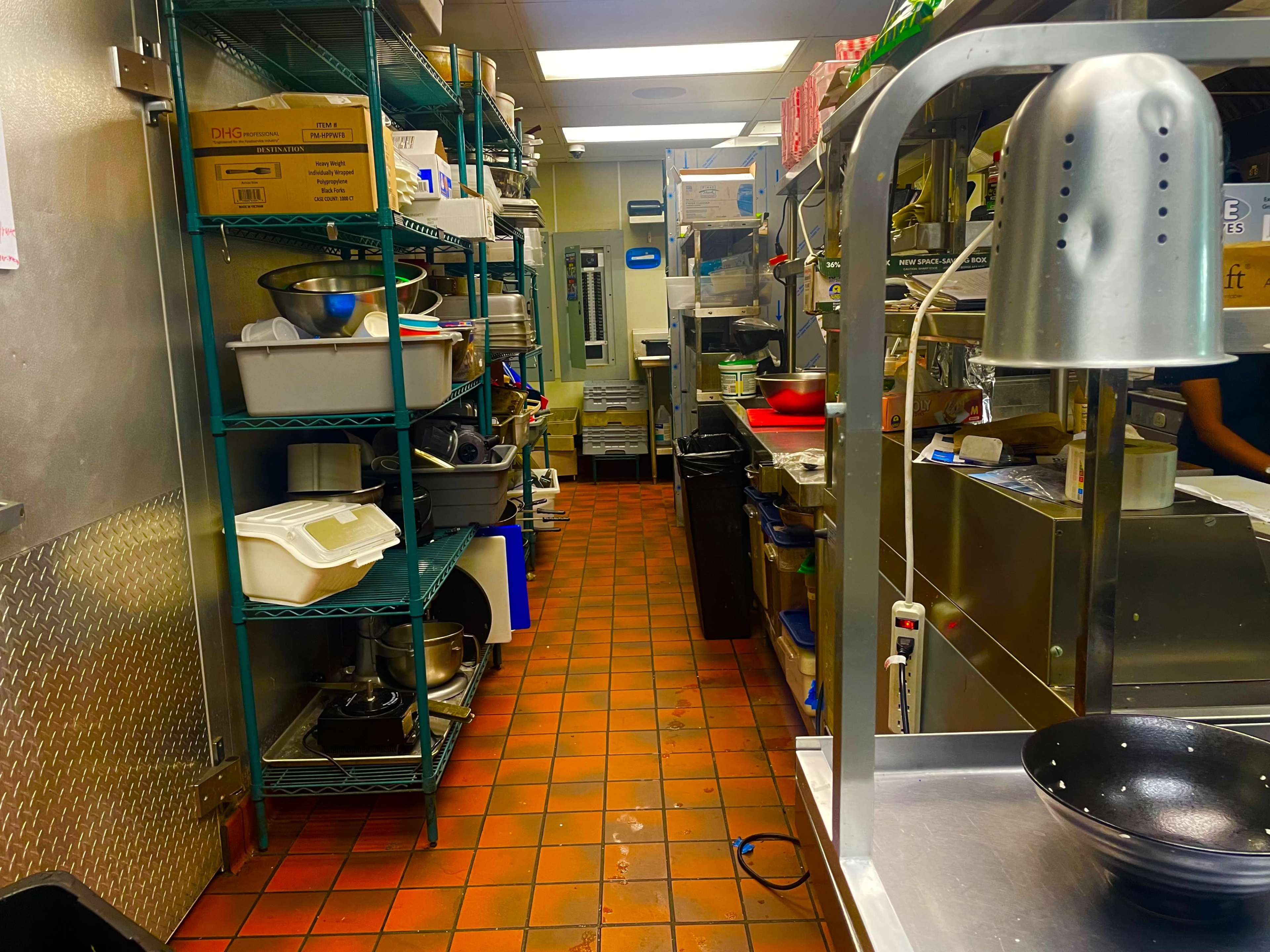 A commercial kitchen with shelves filled with various cooking utensils and containers, along a tiled floor.