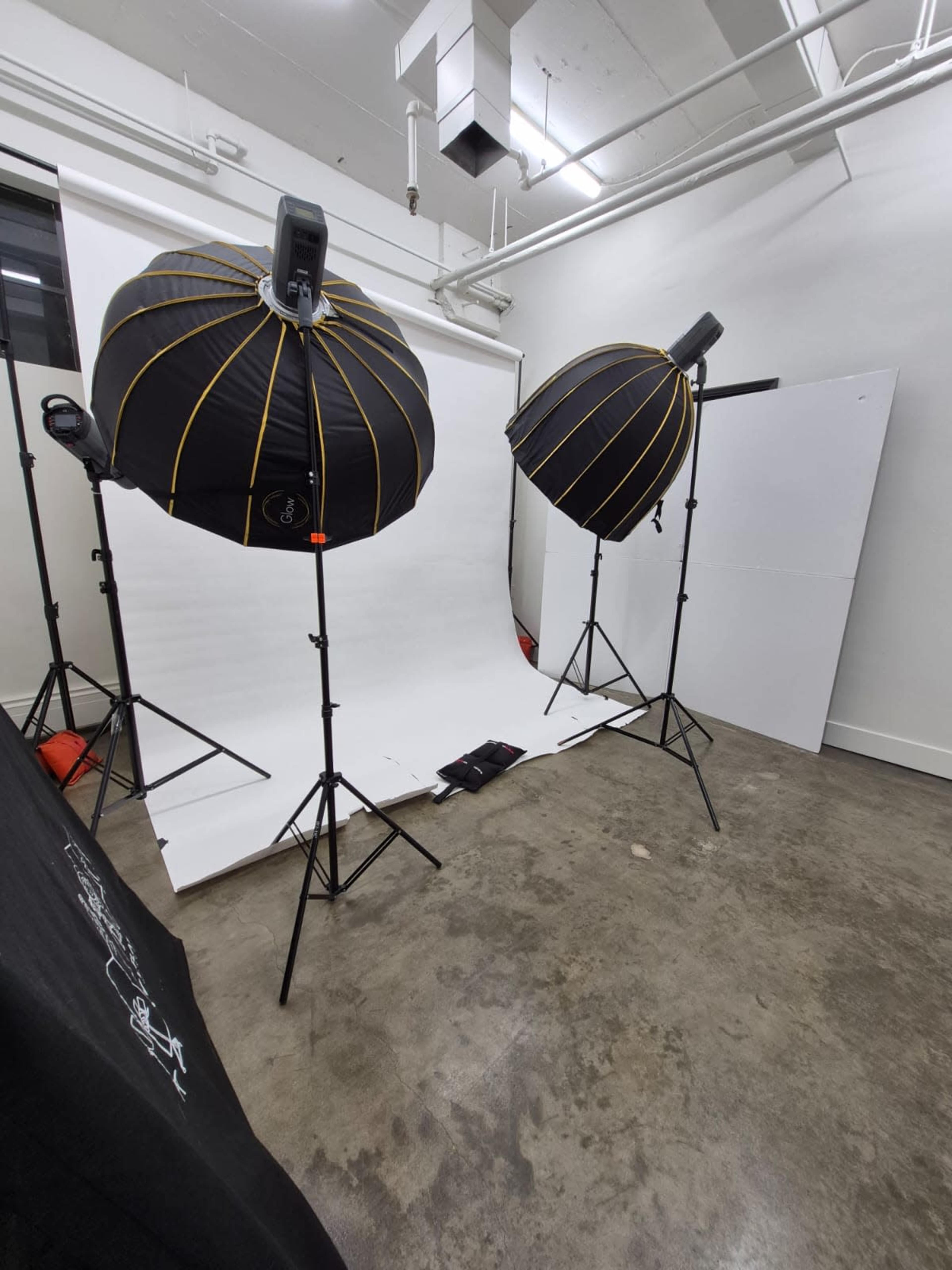 The image shows a photo studio setup with two large softbox lights facing a plain white backdrop.
