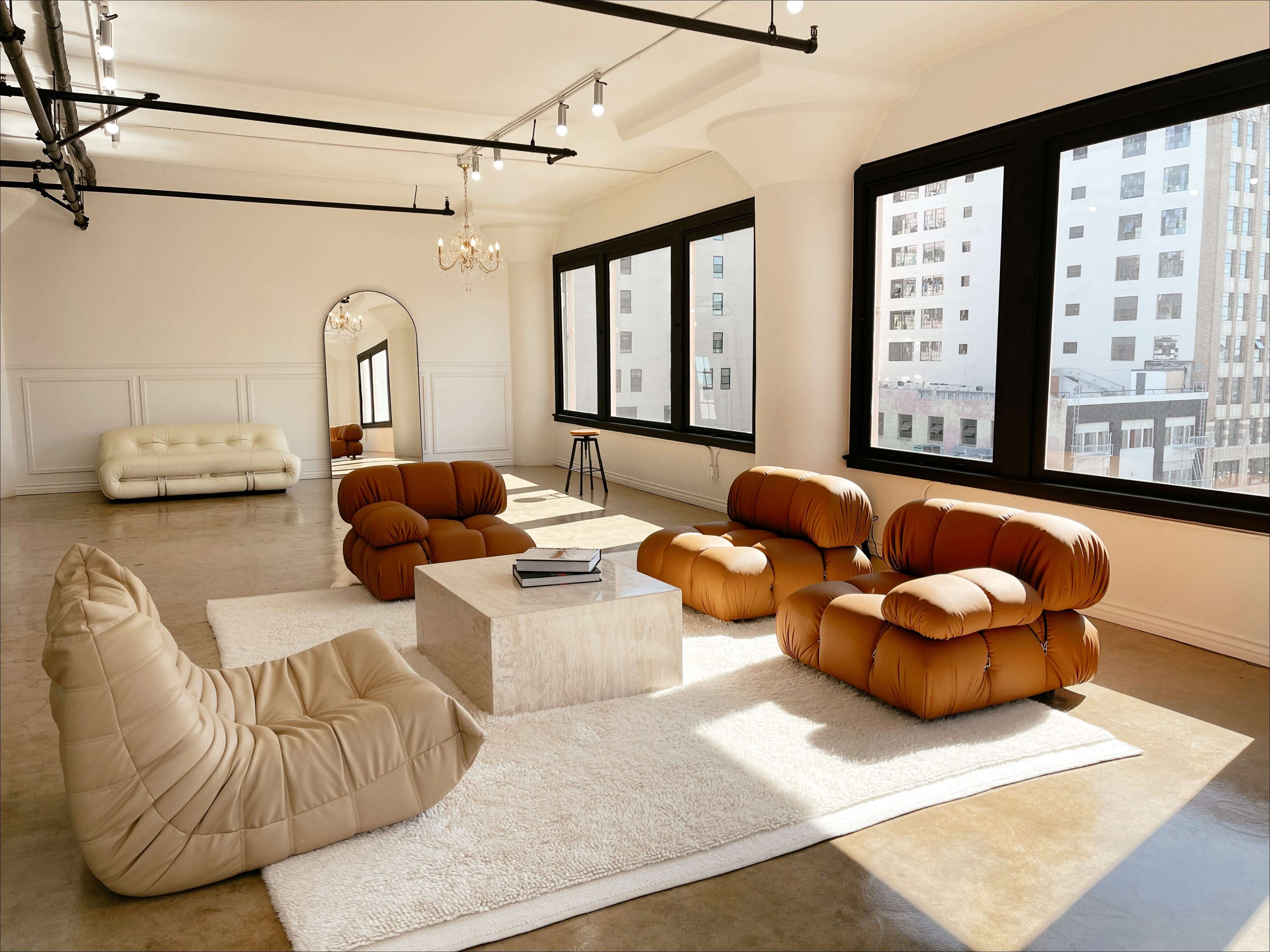 The spacious room features contemporary furniture, including a large coffee table and several uniquely shaped sofas, illuminated by natural light from large windows.