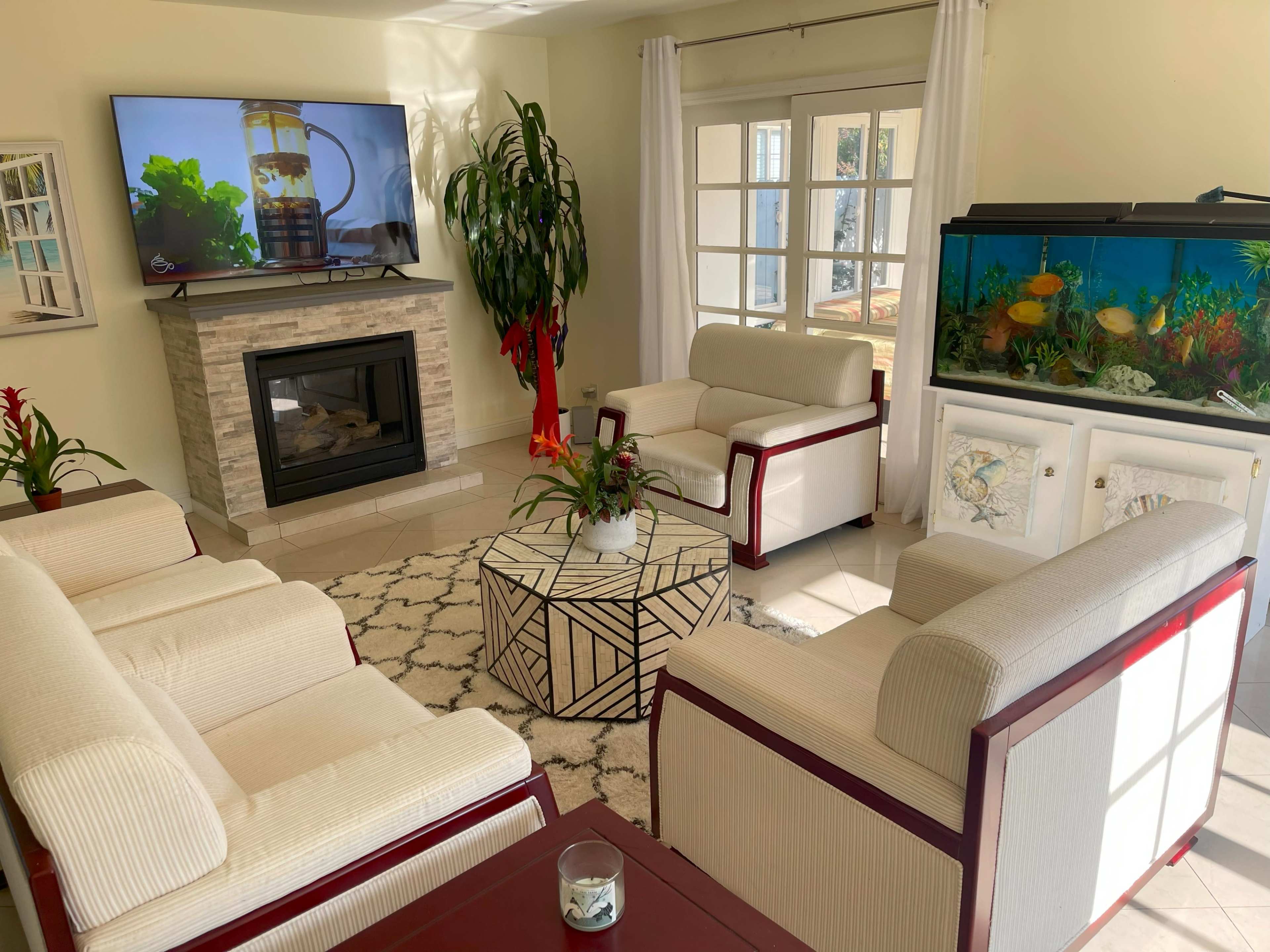 A living room with a fireplace, a large television mounted on the wall, a fish tank, and seating arranged around a geometric coffee table.