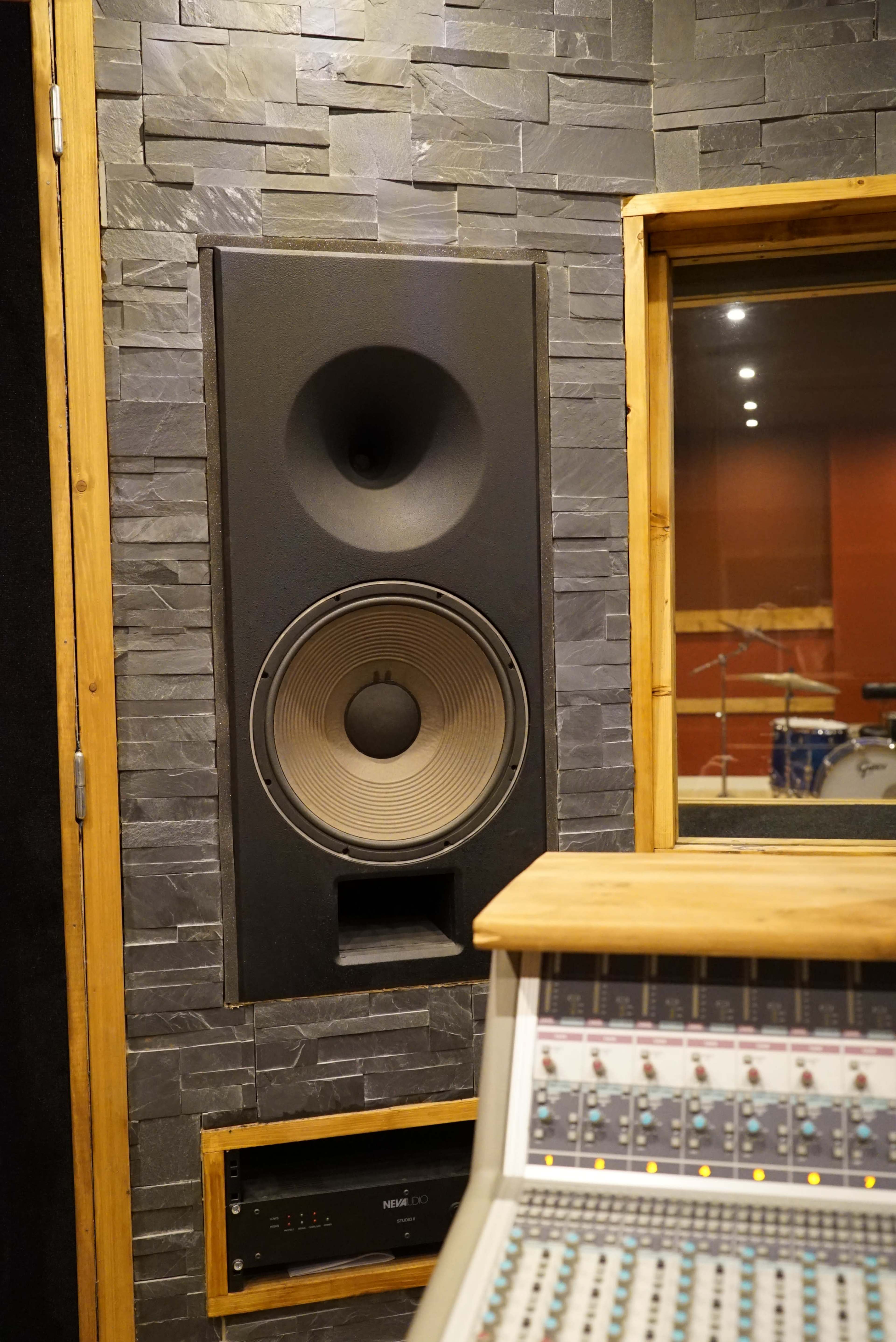 A large speaker integrated into a stone wall, with a mixing console positioned in the foreground.
