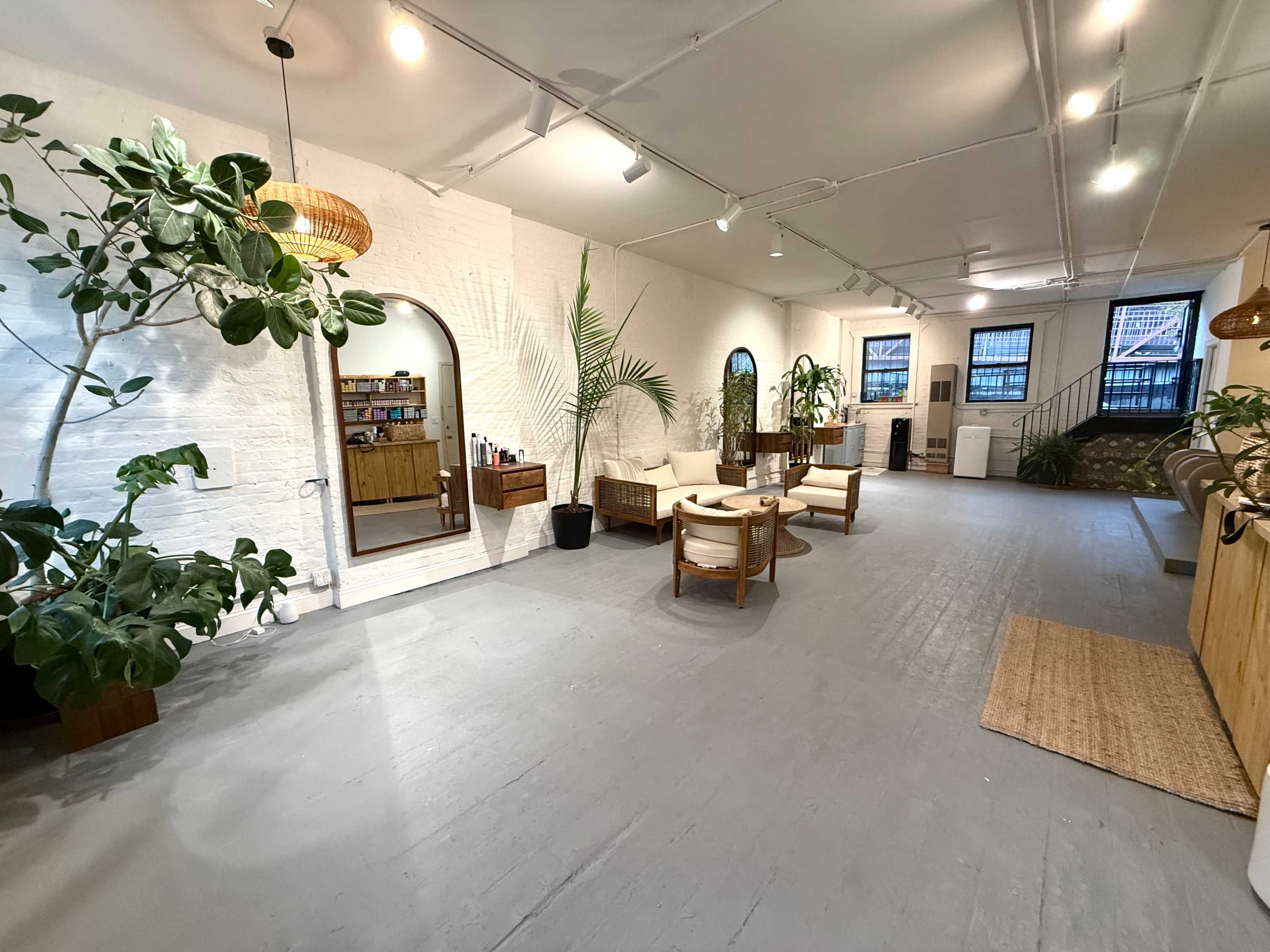 The image shows an interior space featuring plants, a seating area with round tables, and a decorative mirror against a brick wall.