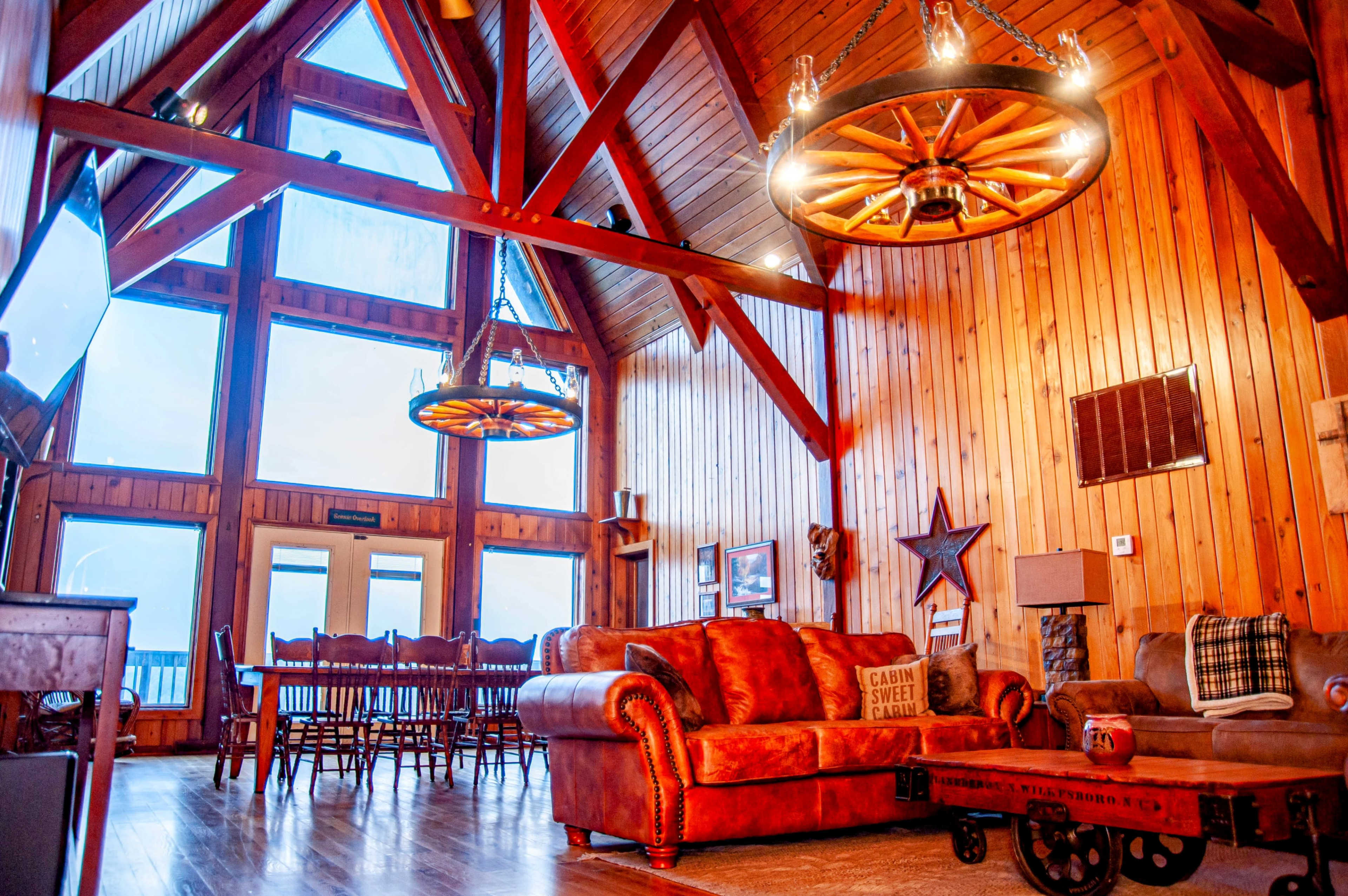 A spacious living area with high wooden ceilings, large windows, and rustic furniture.