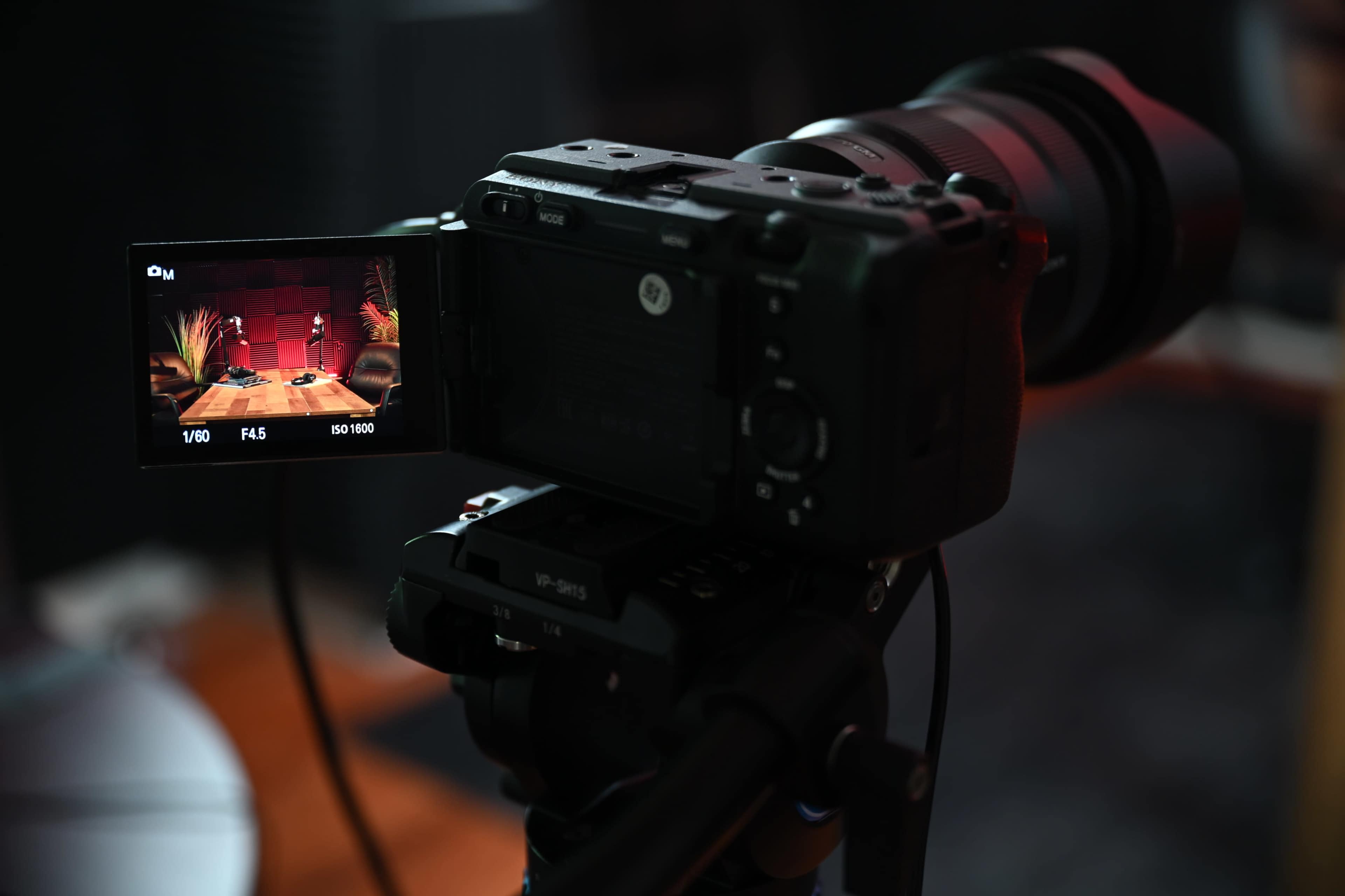 A camera mounted on a tripod displays a scene on its screen, featuring a table with decorative items in a dimly lit environment.