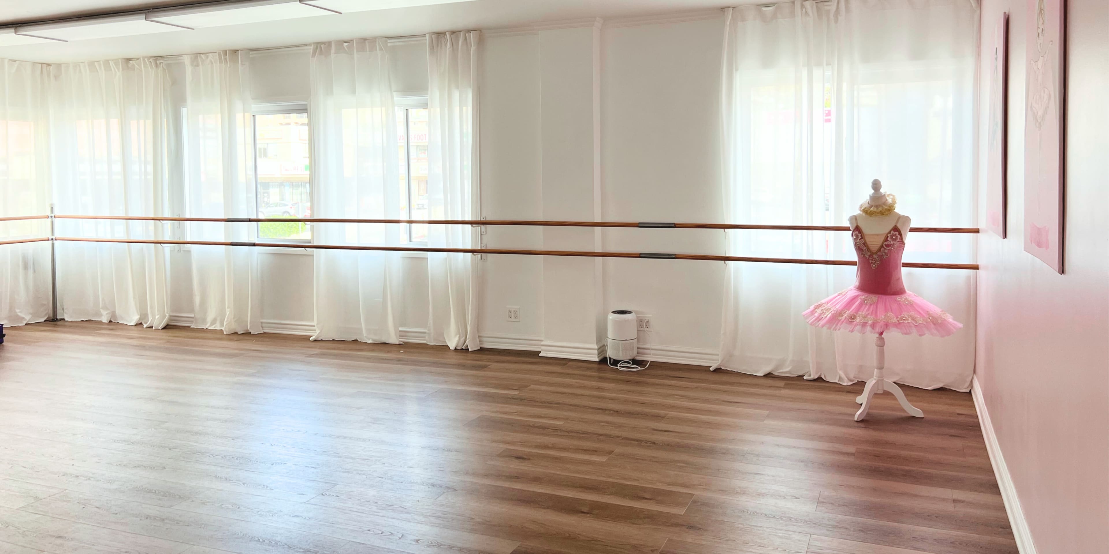 The image shows a dance studio with wooden flooring, large windows covered by white curtains, and a ballet tutu on a mannequin.