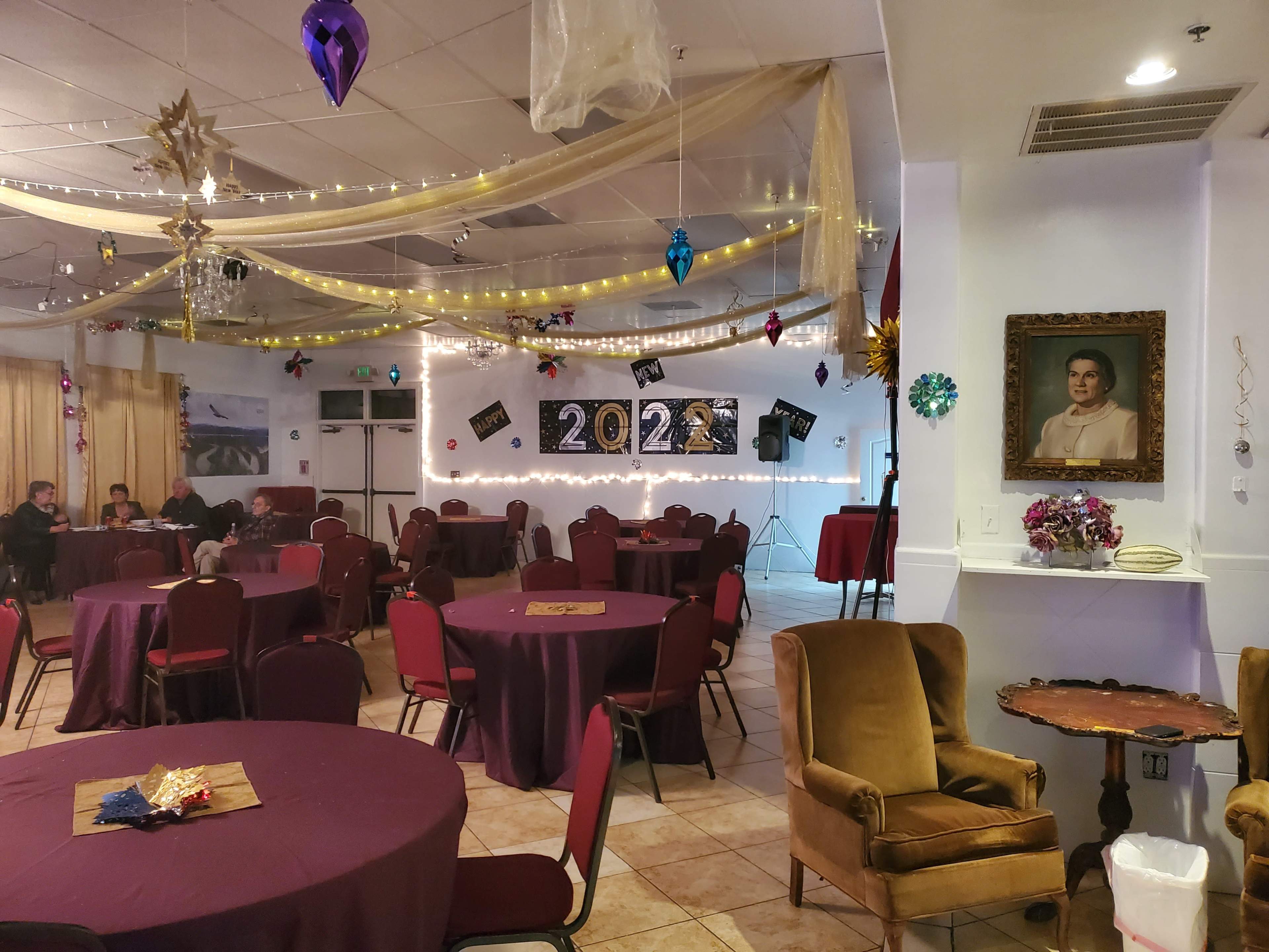 A banquet hall decorated for a New Year's celebration, with tables covered in burgundy cloth, a "2023" display on the wall, and festive decorations hanging from the ceiling.