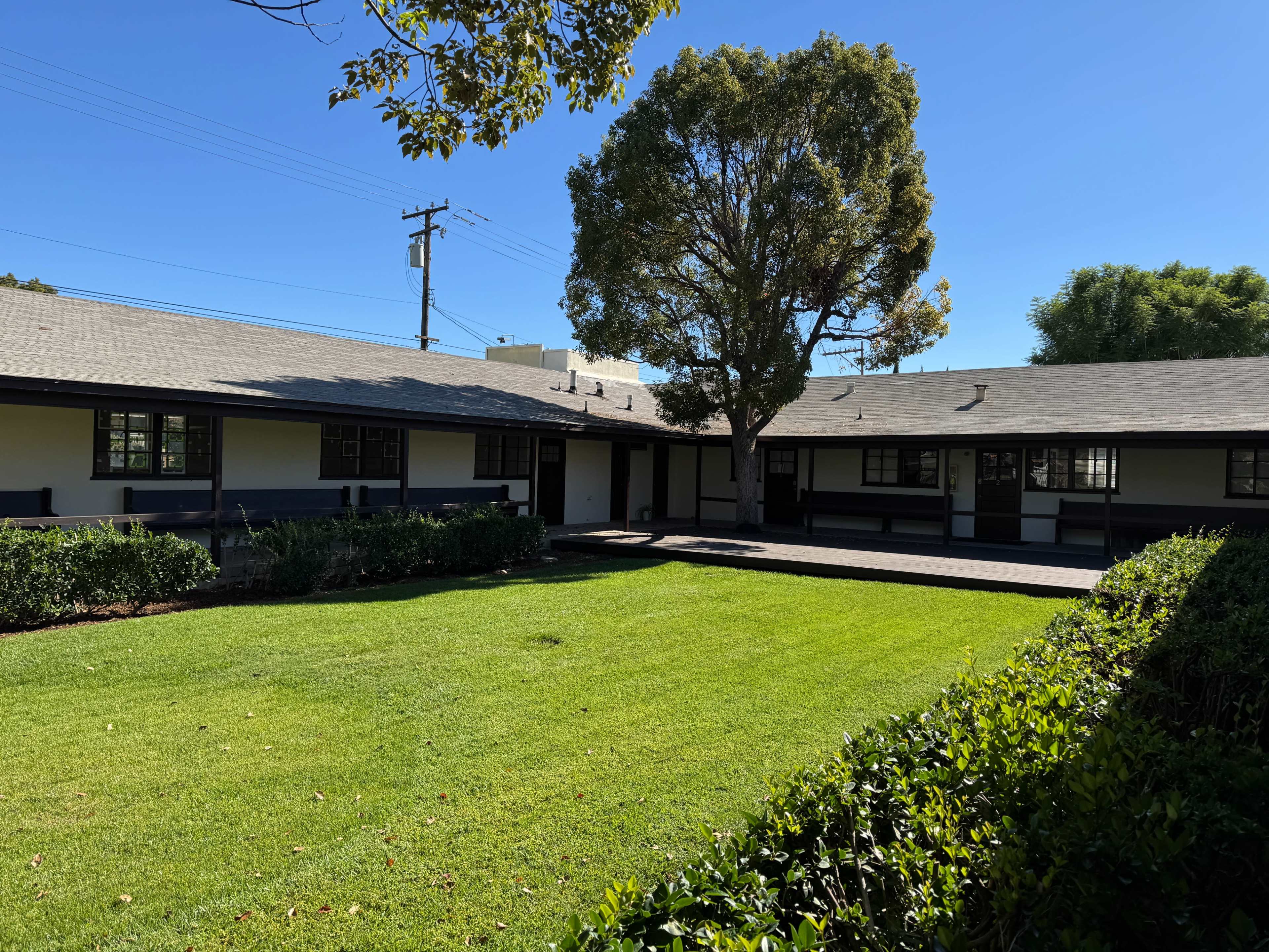 The image shows a well-maintained courtyard surrounded by two buildings with a gray roof and green landscaping under a clear blue sky.